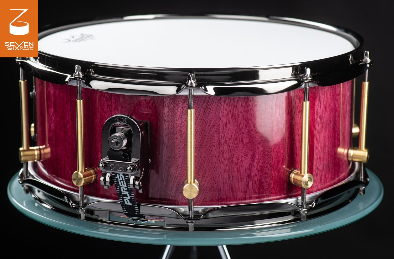 Handmade snare drum with a glossy purpleheart wood shell, brass tube lugs, black nickel hoops, and a DW throw-off.