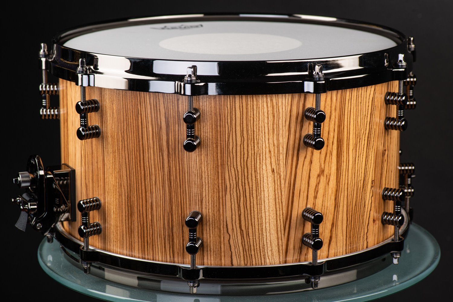 Handmade snare drum in natural-finish zebrawood, accented with black nickel hoops, dual lugs, and throw-off.