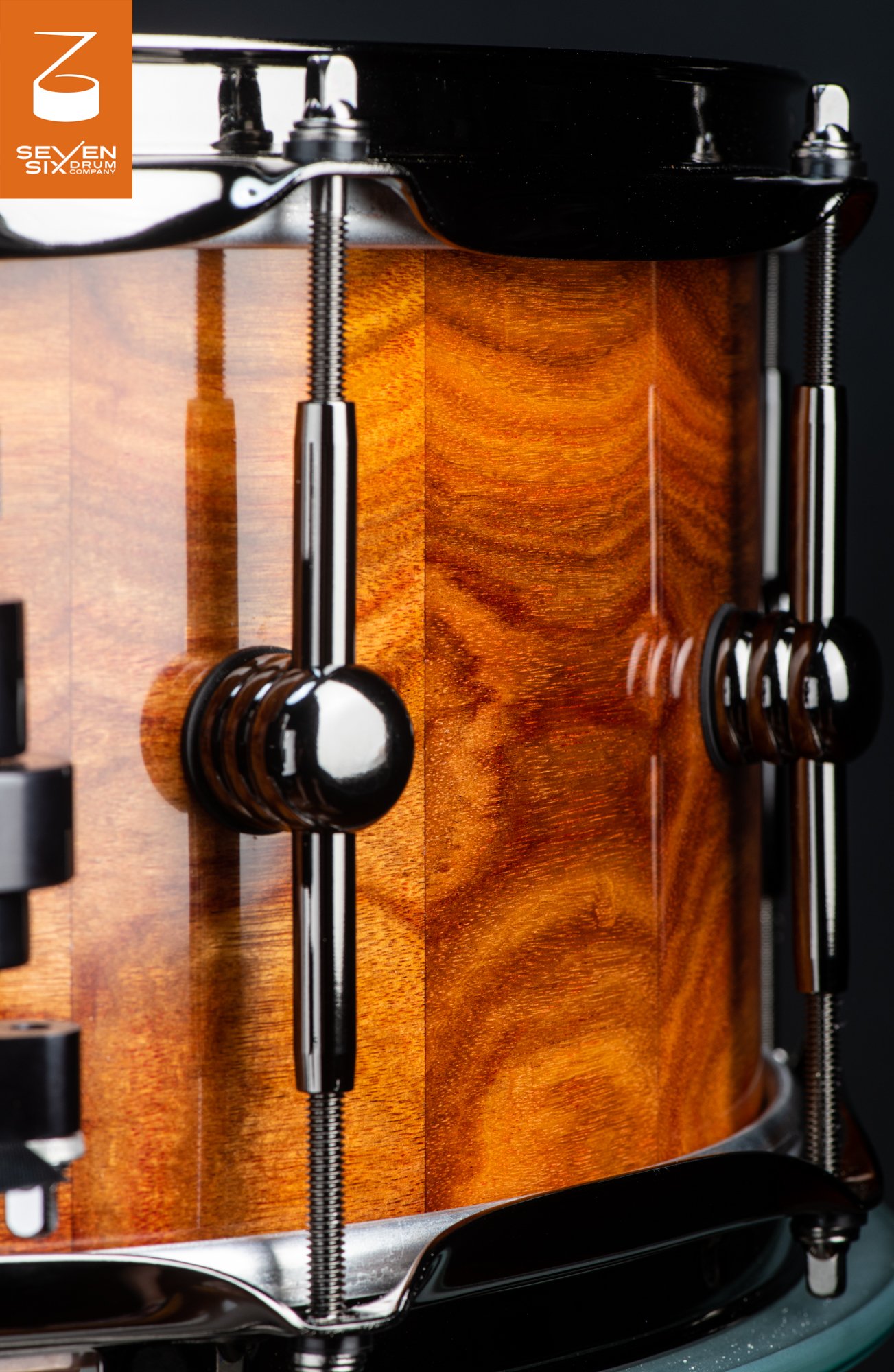 Handmade snare drum featuring a high-gloss figured wood shell, black nickel tube lugs, and matching hoops.