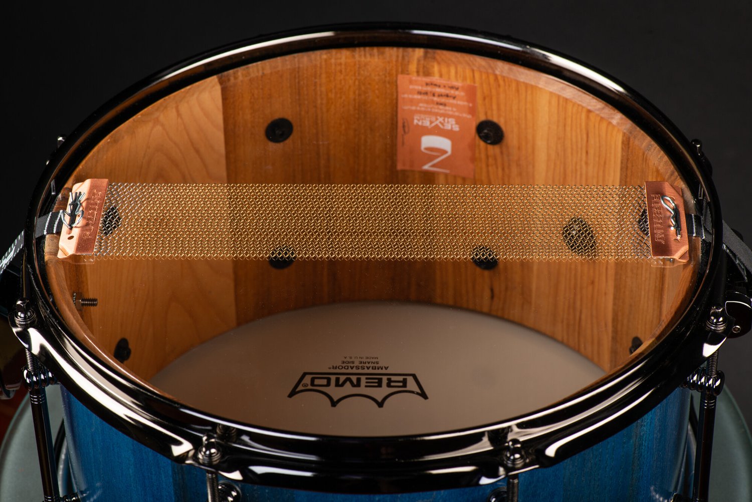 Bottom view of a blue wood snare drum with a natural interior shell, black metal hoop, and brass PureSound snare wires.