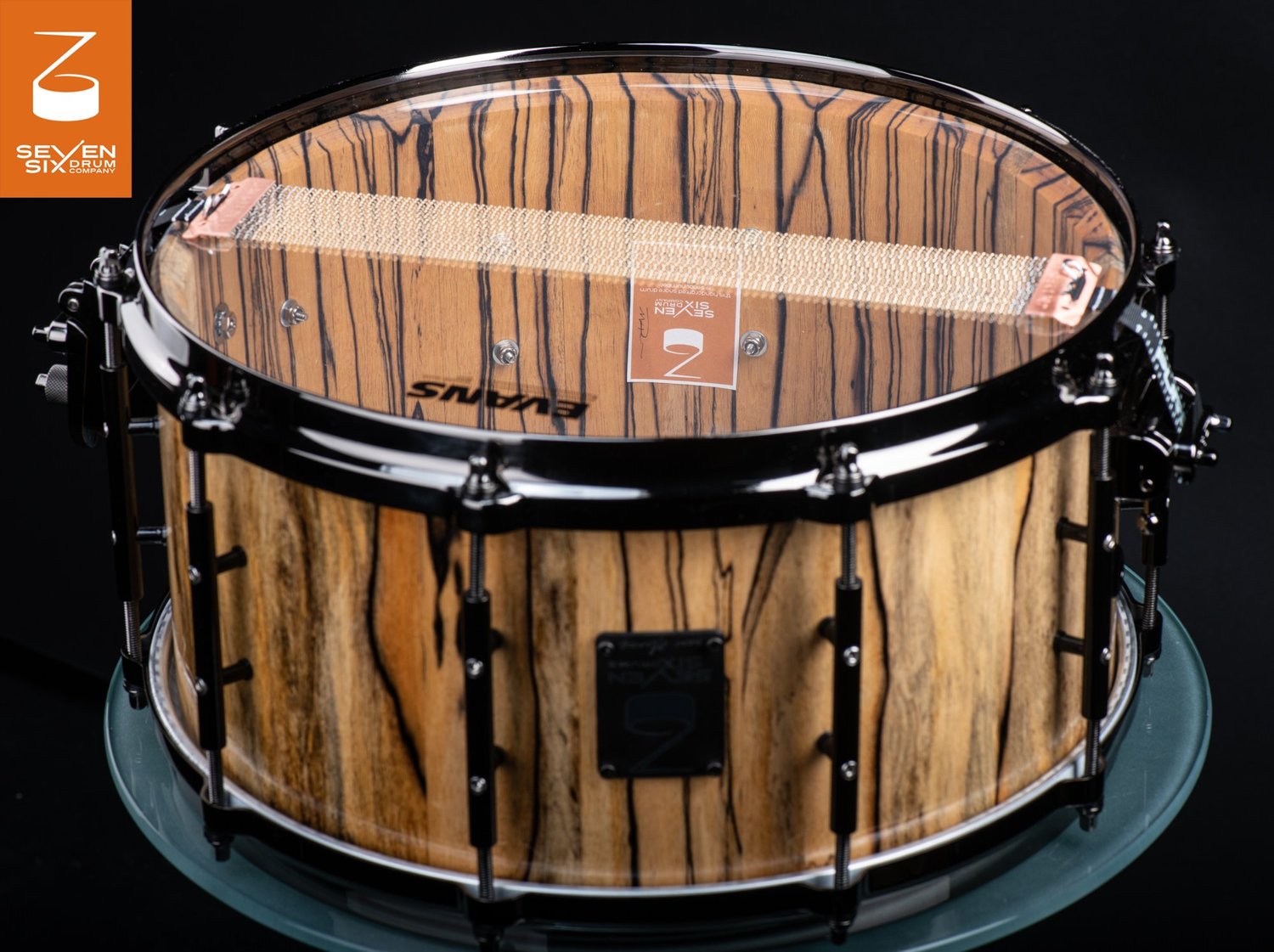 Handmade snare drum featuring natural striped ebony wood with gloss black hoops, lugs, and snare wires.