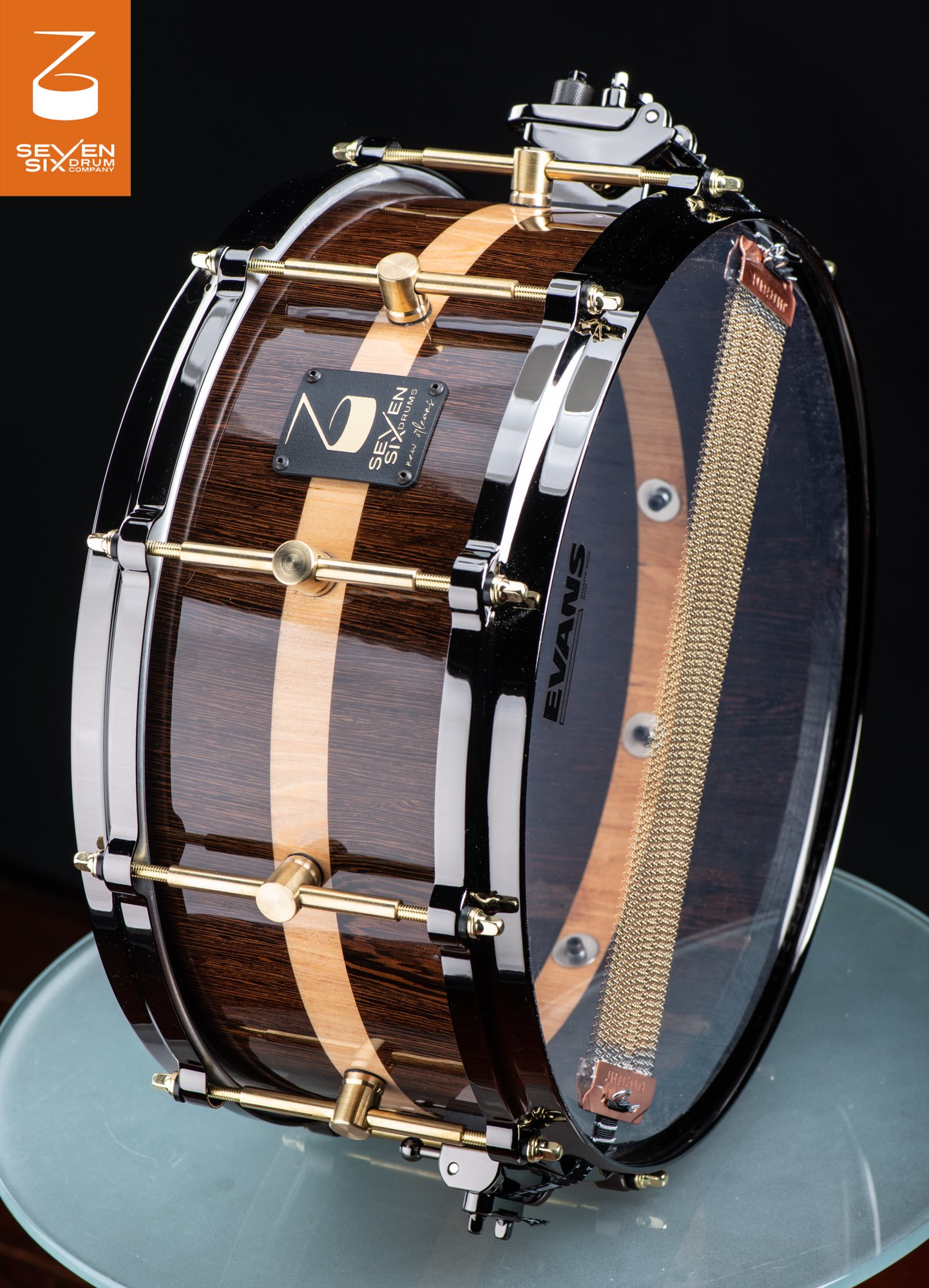 Handmade snare drum with a high-gloss dark wood shell, blonde center stripe, brass lugs, and black hoops.