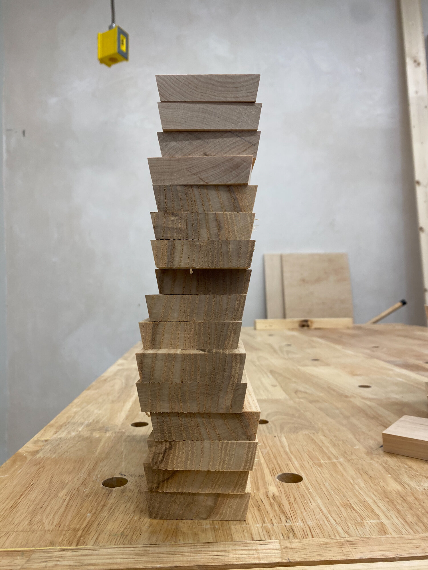 A stack of unfinished, beveled wooden drum staves sits on a workshop bench awaiting shell assembly.