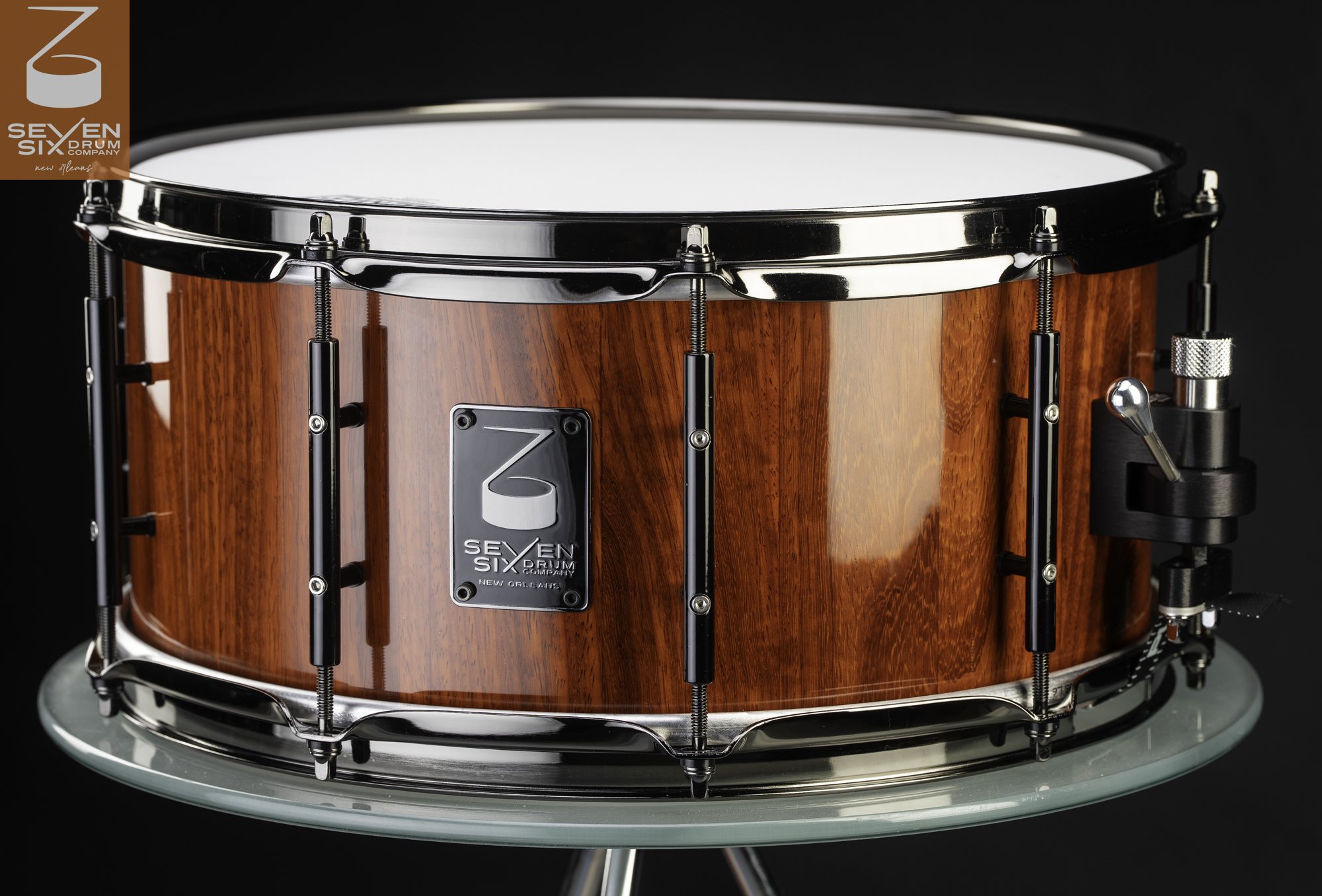 Glossy reddish-brown wood snare drum with black tube lugs, chrome hoops, and a side-lever throw-off.
