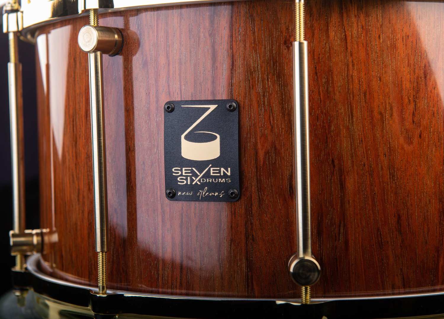 Handmade wood snare drum with a glossy brown finish, brass tube lugs, and a black Seven Six Drums badge.