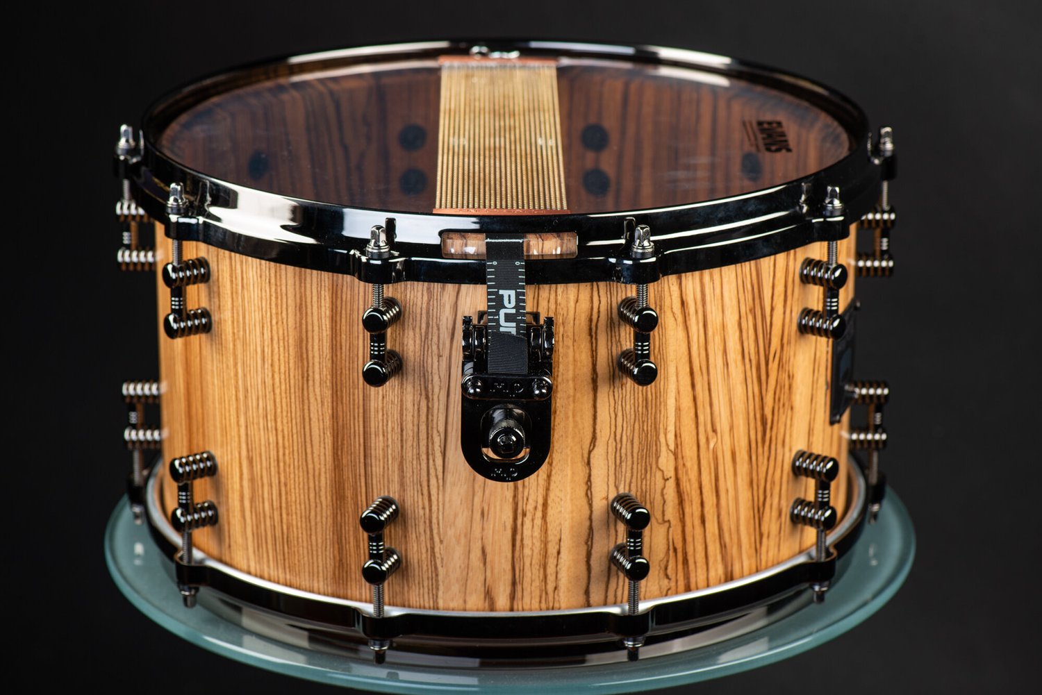 Handmade natural zebrawood snare drum featuring gloss black hardware, dual lugs, and bottom snare wires.