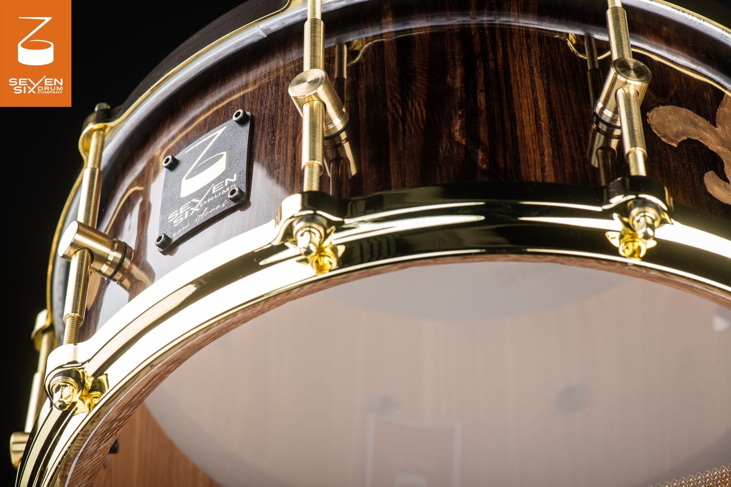 Handmade snare drum with a glossy dark wood shell and polished brass lugs and hoops.