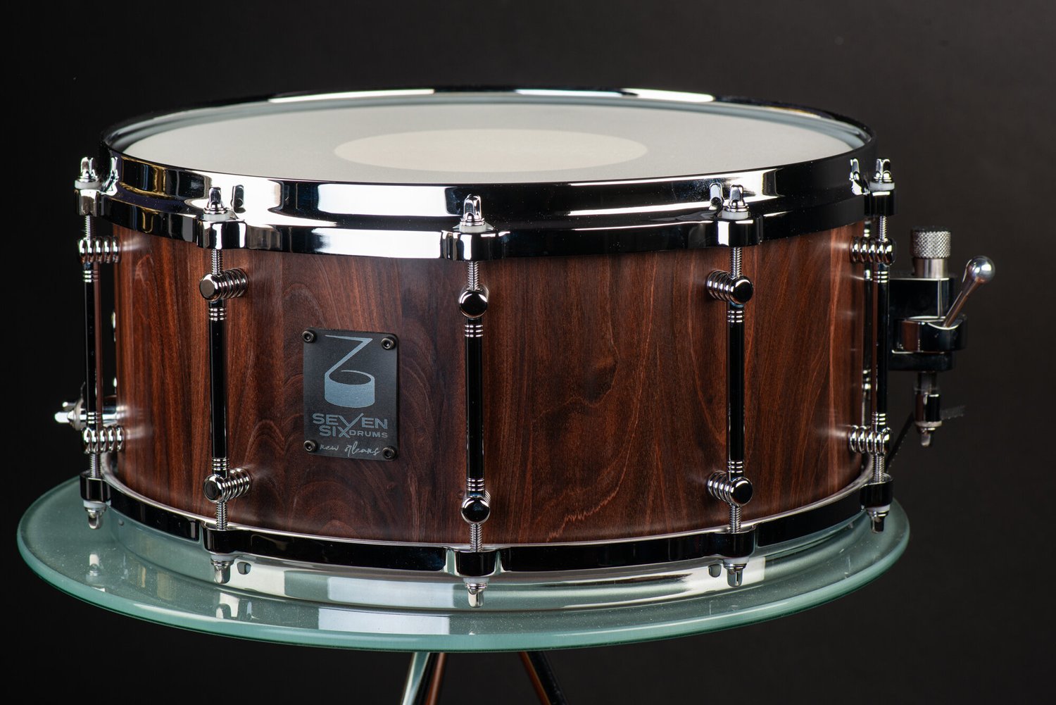Snare drum featuring a dark satin wood shell, polished chrome tube lugs, and a chrome side throw-off.