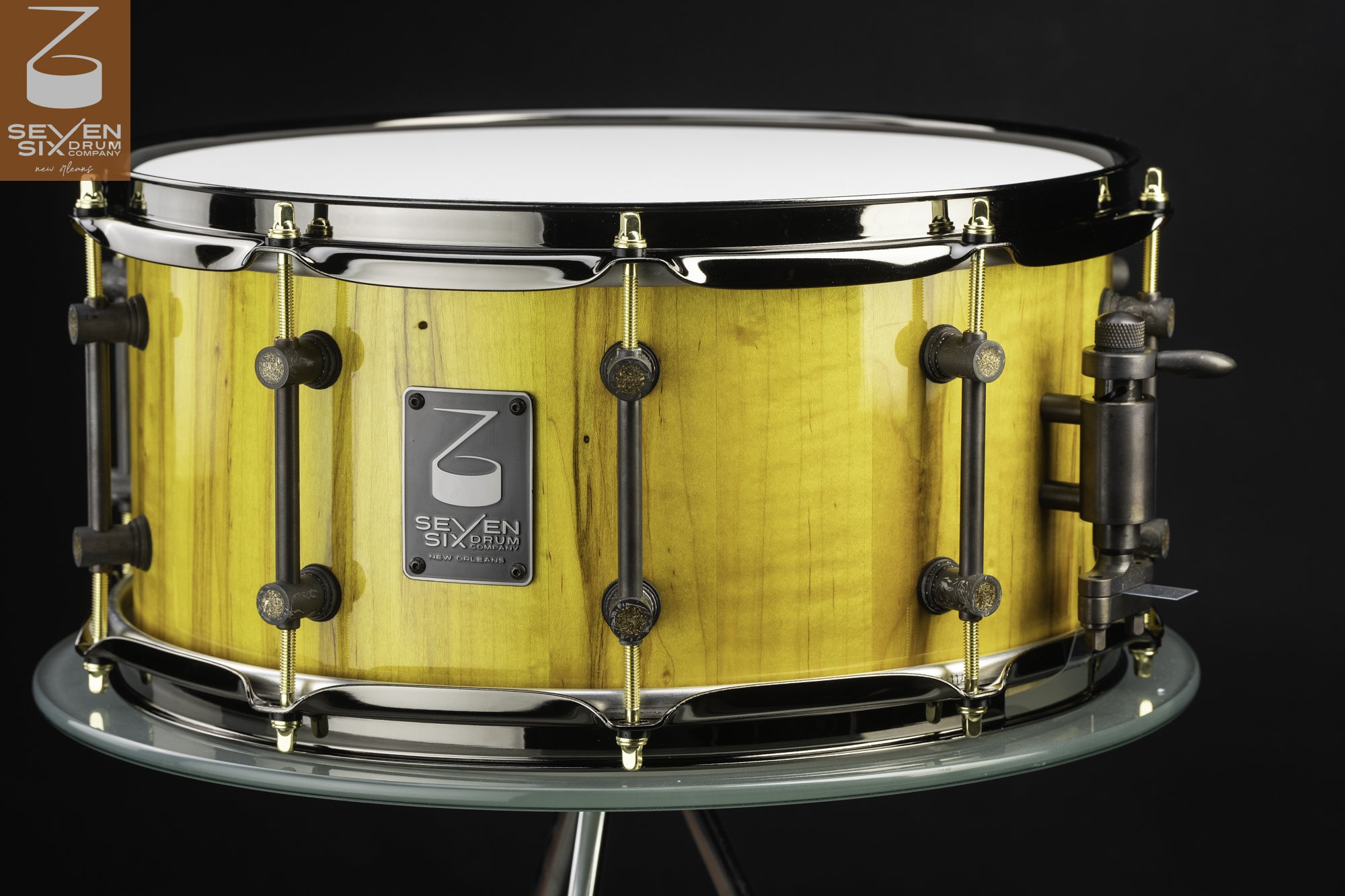 Handmade snare drum with a glossy yellow wood shell, dark tube lugs, gold tension rods, and chrome hoops.