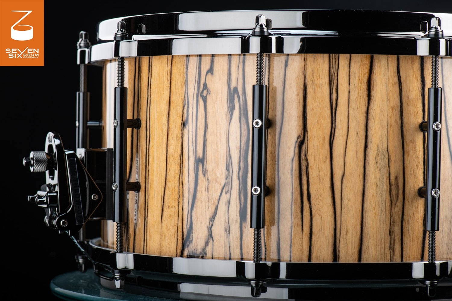 Handmade snare drum with a glossy zebrawood shell, black nickel hoops, tube lugs, and a DW throw-off.