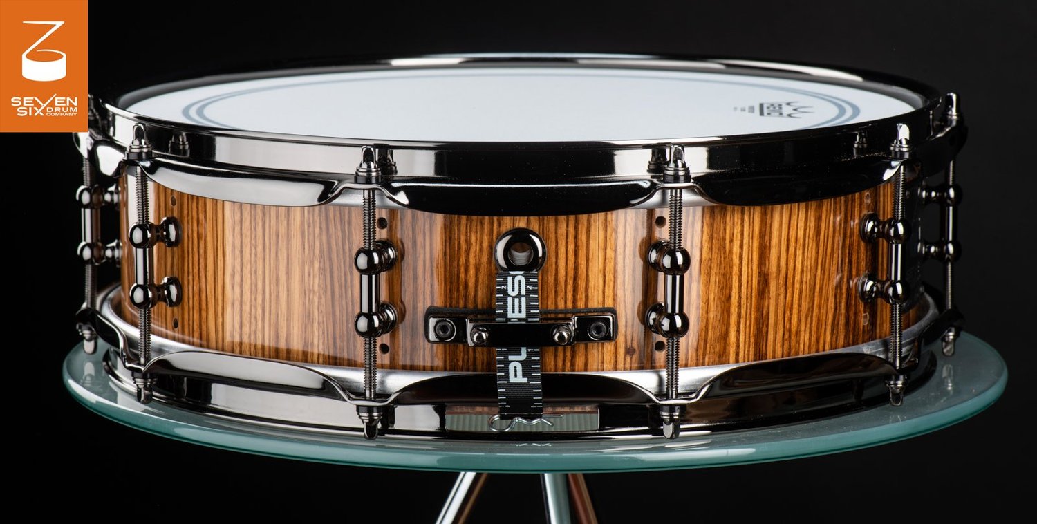 Handmade glossy zebrawood snare drum with black nickel hoops and tube lugs.