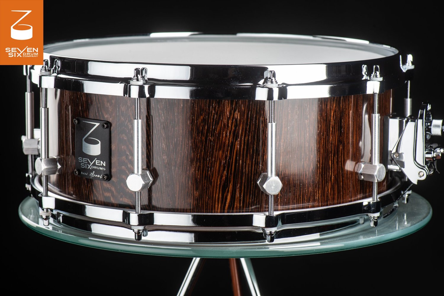 Handmade snare drum featuring a glossy dark brown wood shell, polished chrome hoops, and brushed metal lugs.