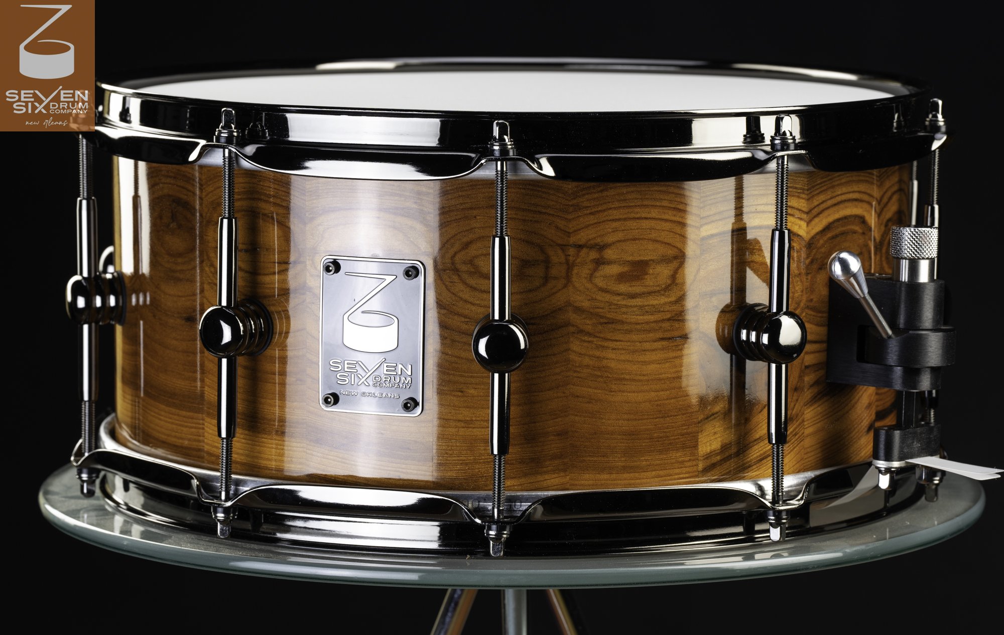 High-gloss natural wood snare drum featuring black nickel hoops, center-mounted lugs, and a throw-off.