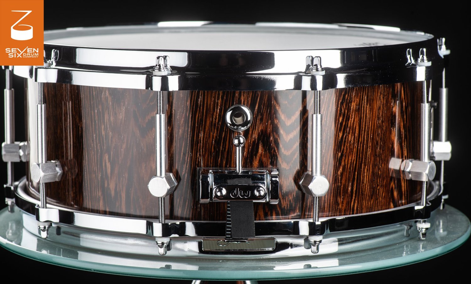 Handmade snare drum featuring a glossy dark wood grain shell, polished chrome rims, hex lugs, and a DW strainer butt plate.