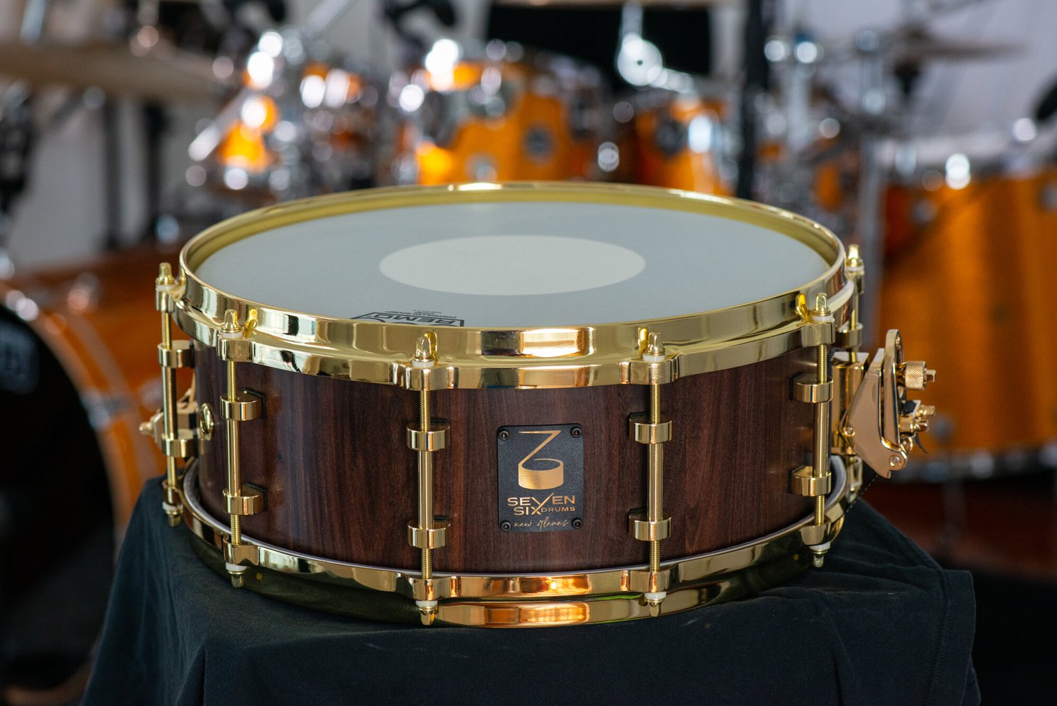 Handmade snare drum with a dark satin wood shell and polished brass hoops, lugs, and throw-off.