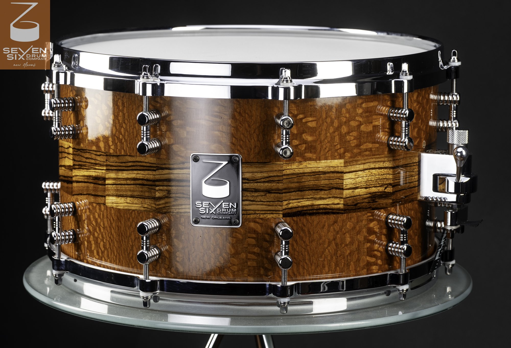 Handmade snare drum with a high-gloss segmented wood shell, zebrawood center stripe, and polished chrome hardware.