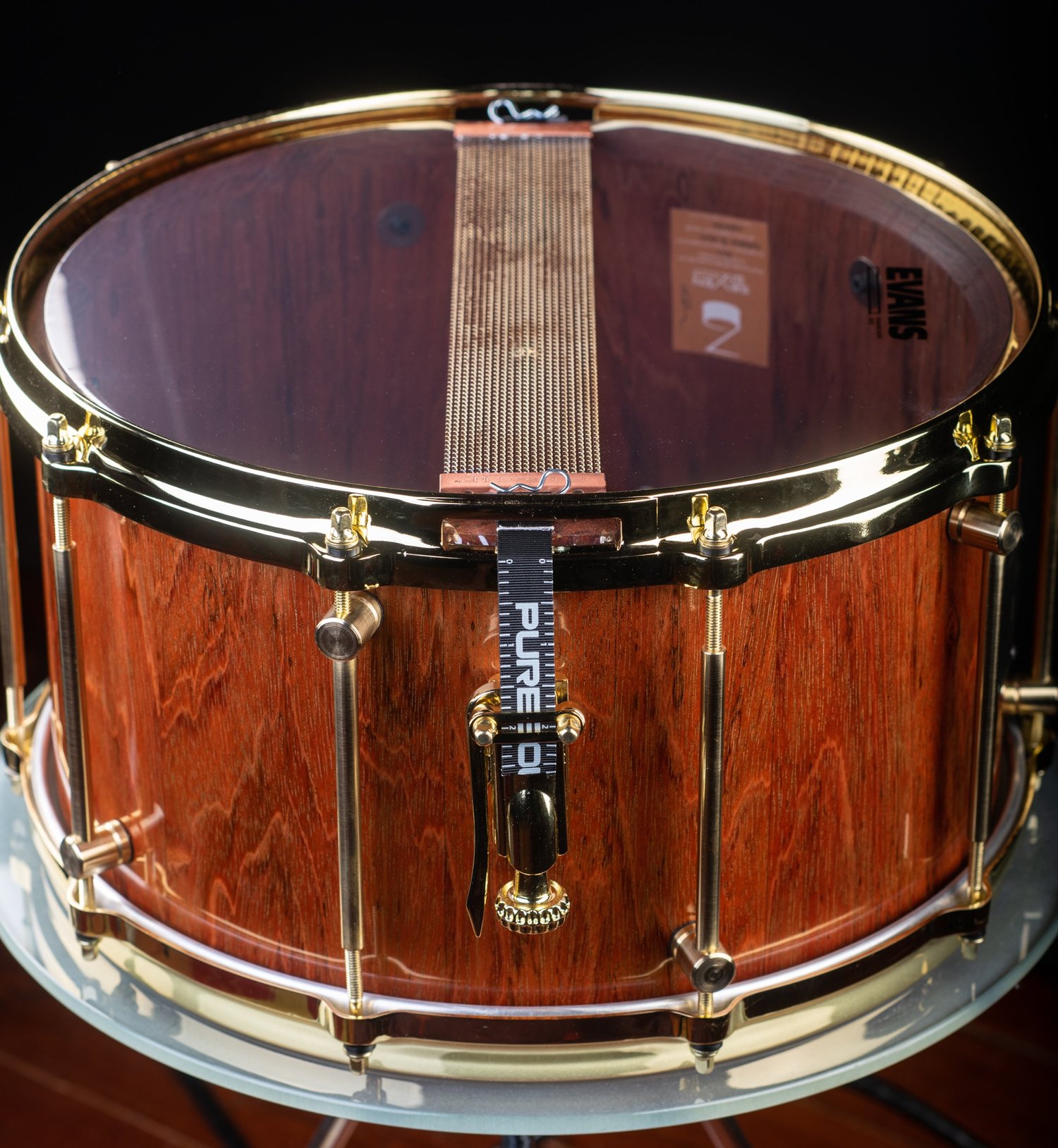 Handmade snare drum with a polished natural wood shell, gleaming gold hoops, brass tube lugs, and bottom snare wires.