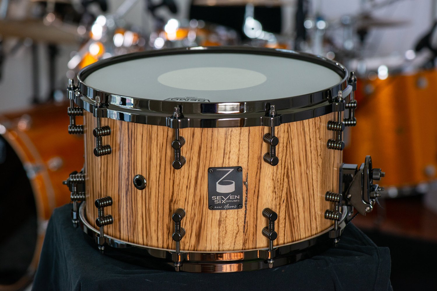 Handmade zebrawood snare drum with a natural finish, black nickel hoops, and matching dual-contact lugs.