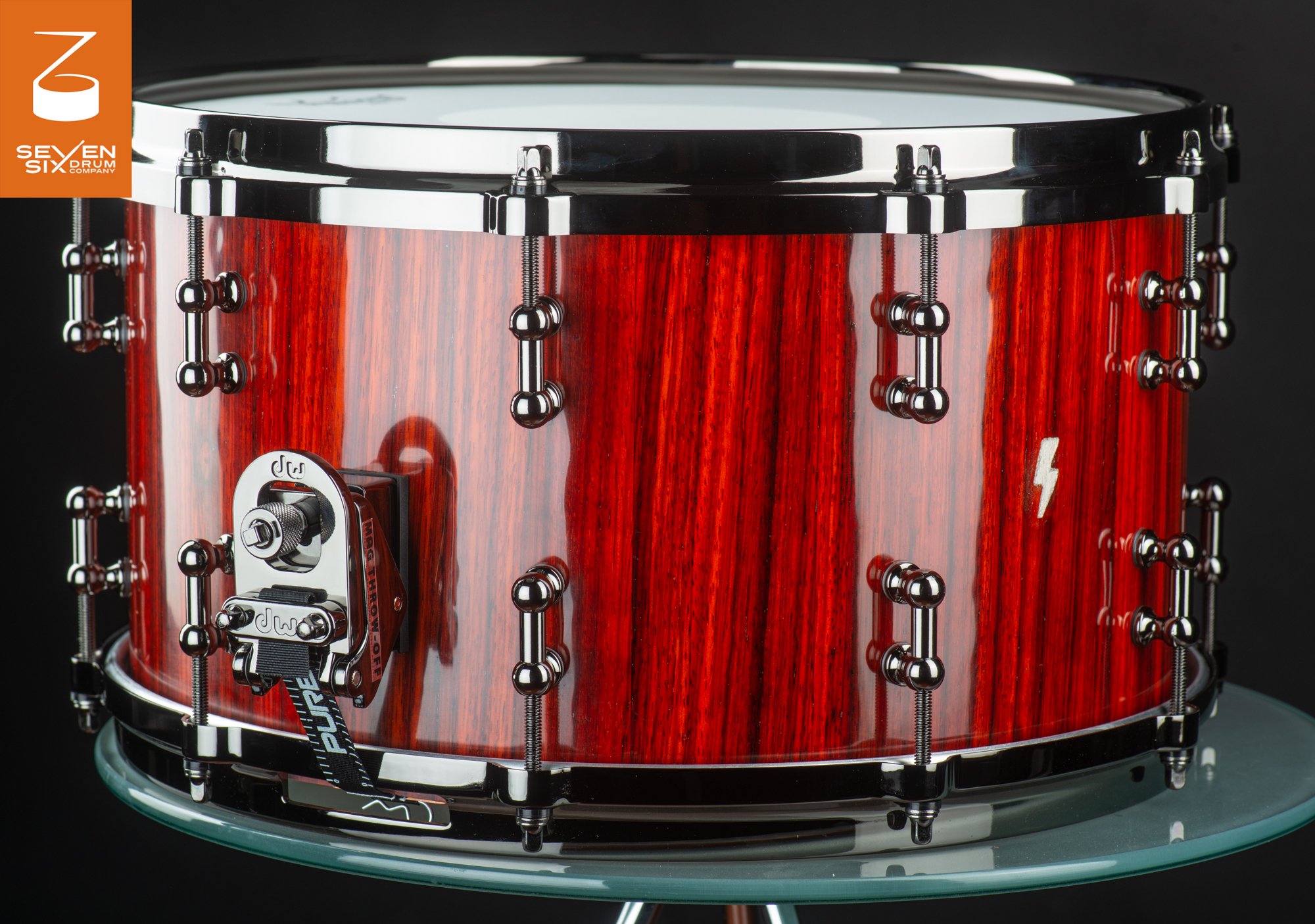 Deep snare drum with a glossy red vertical-grain wood finish, chrome tube lugs, and a DW MAG throw-off.