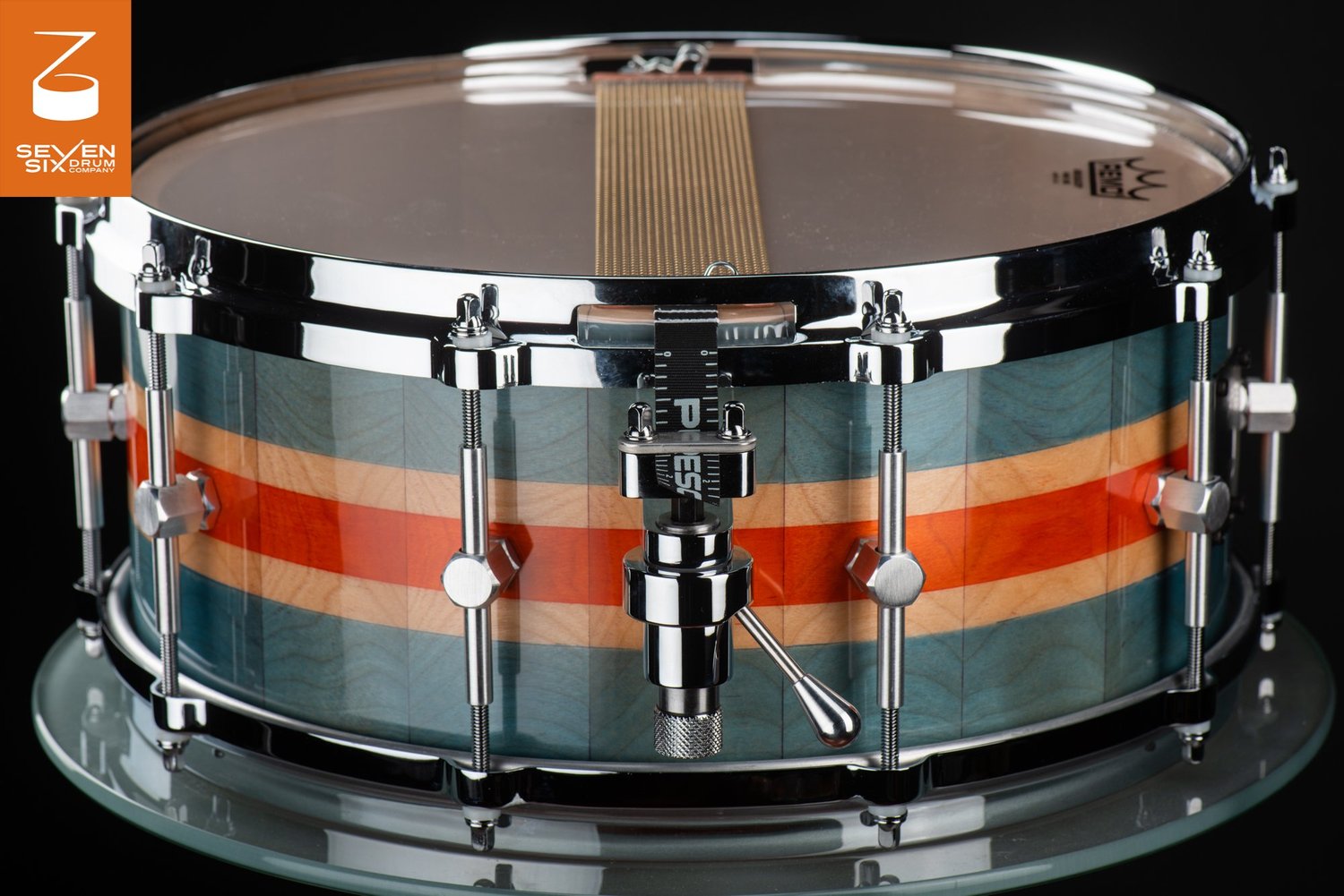 Handmade snare drum with a glossy teal, orange, and maple striped wood shell, chrome hoops, and a snare throw-off.