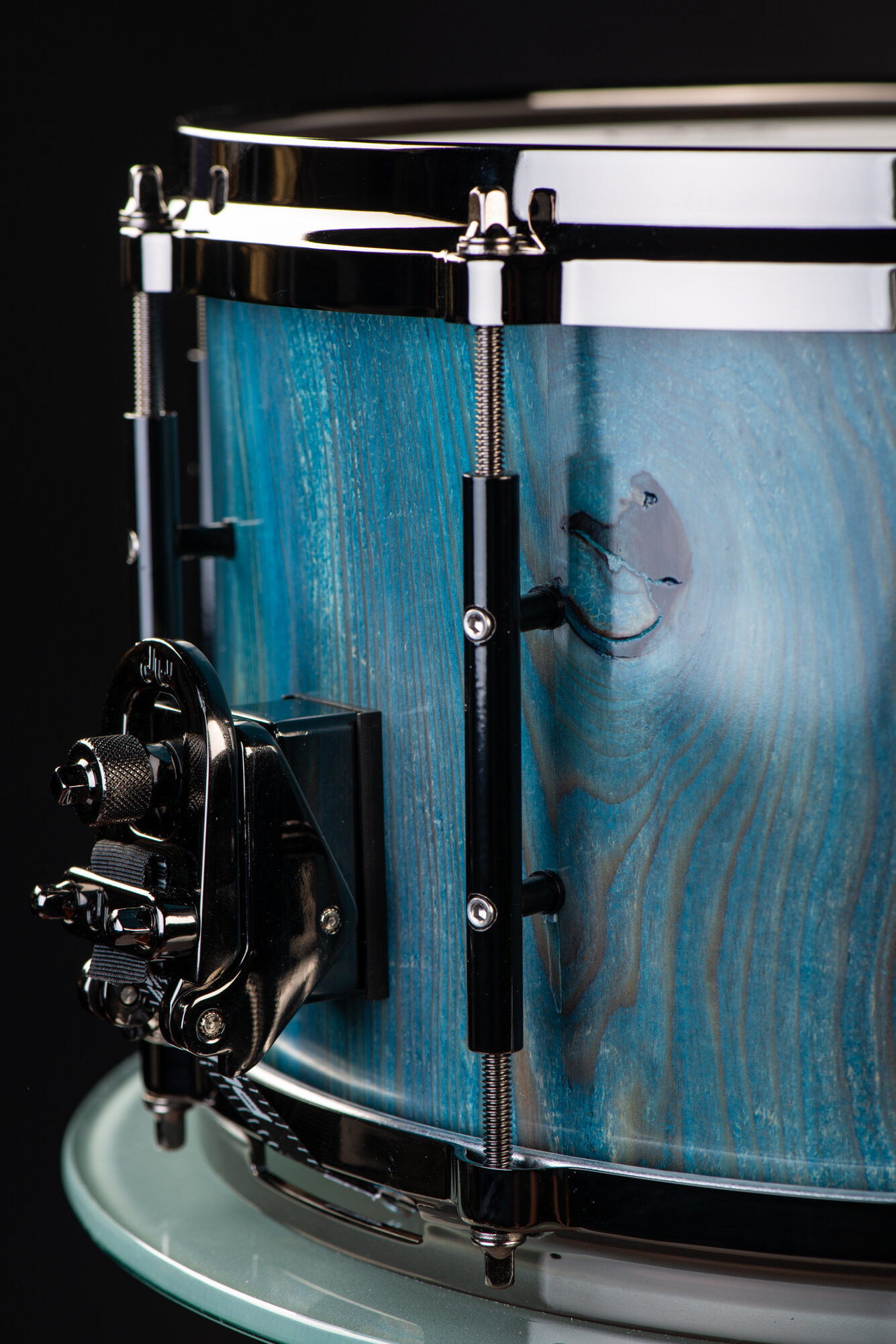 Handmade snare drum with a blue-stained wood grain shell, chrome hoops, black tube lugs, and a snare throw-off.