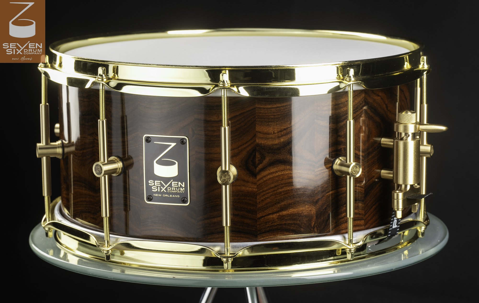 A handmade snare drum features a high-gloss dark wood shell, polished brass hoops, and gold-tone hardware.