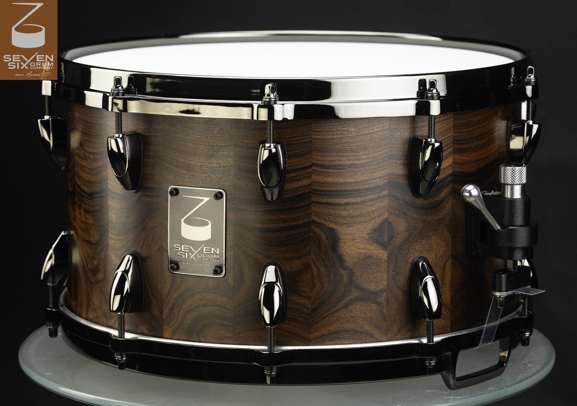 Handmade snare drum in figured dark wood with a satin finish, black nickel hoops, and teardrop lugs.