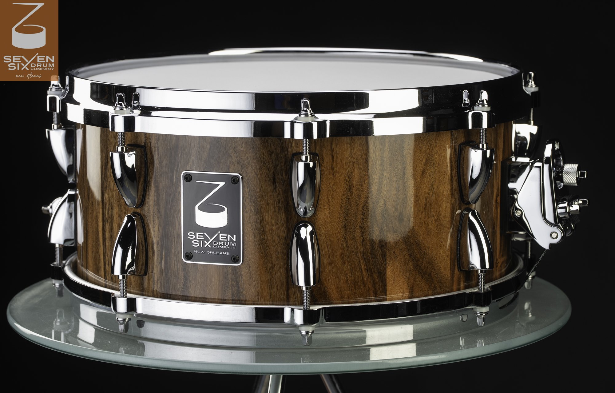 Natural wood snare drum with a high-gloss finish, polished chrome hoops, dual lugs, and a black brand badge.