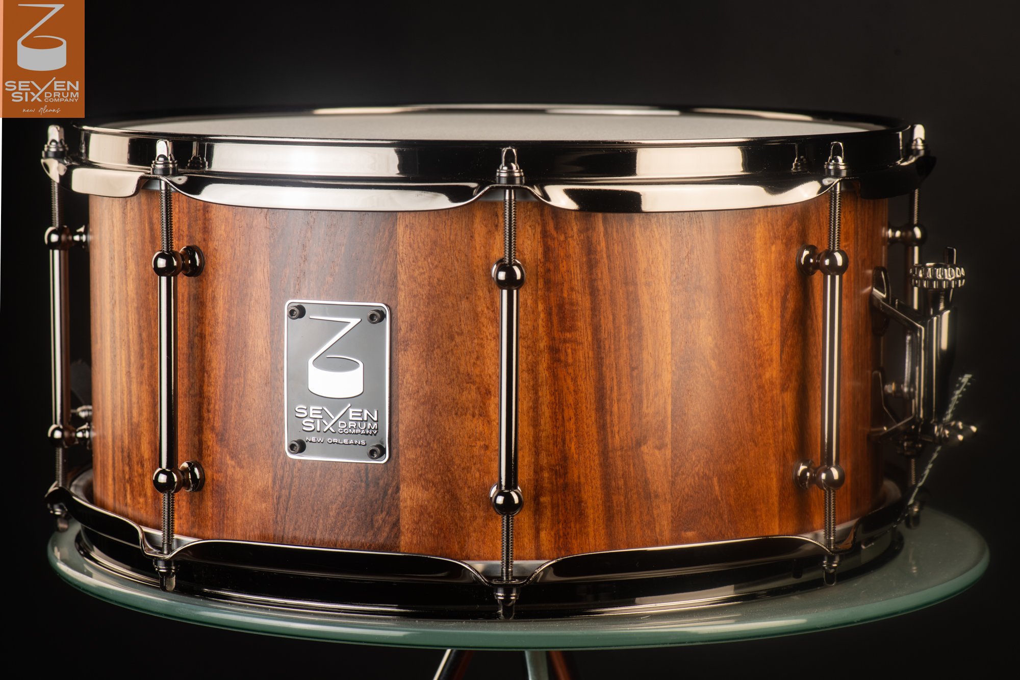 Handmade snare drum crafted from warm, natural-finish wood with sleek black nickel tube lugs and hoops.