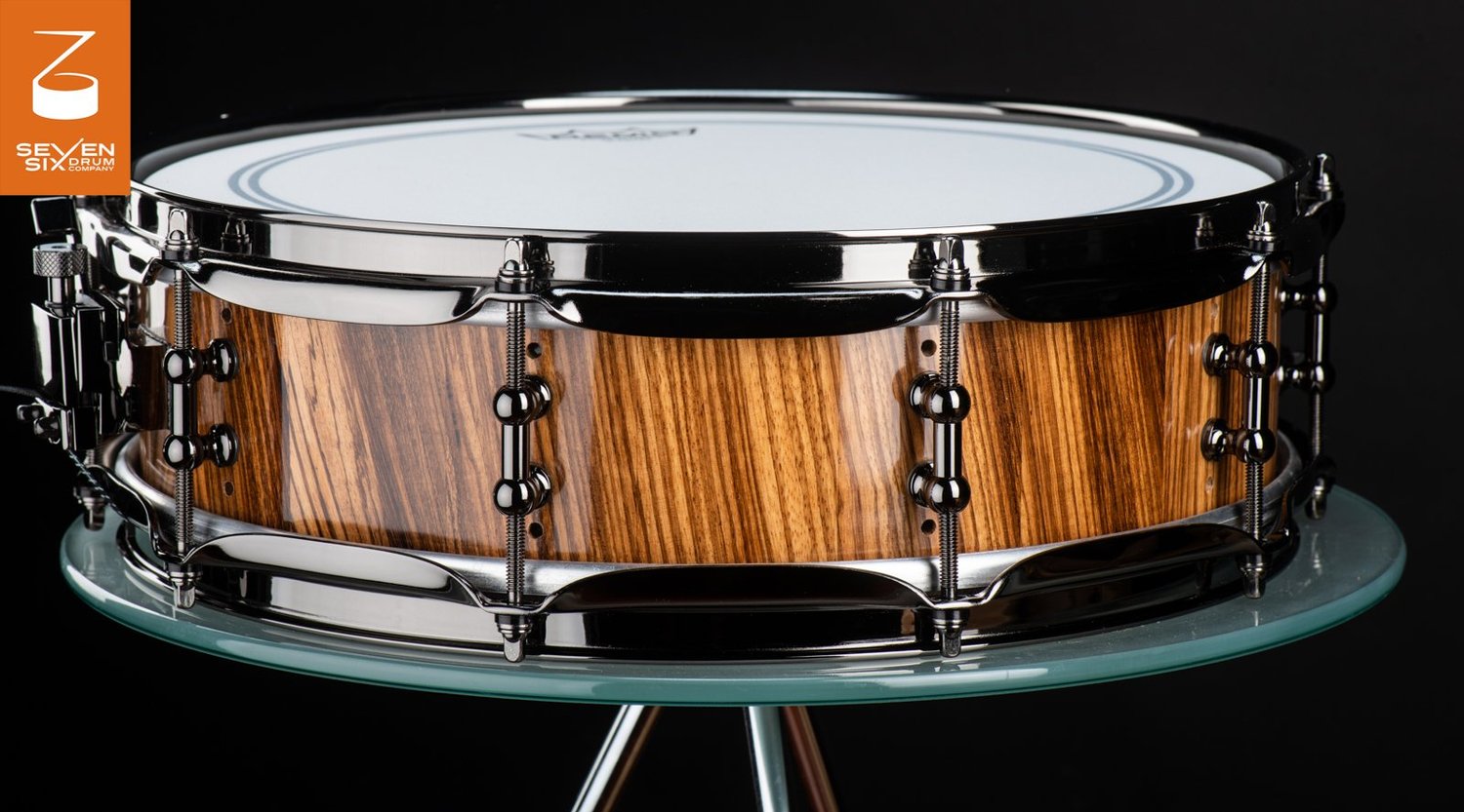 Handmade snare drum featuring a glossy zebrawood shell, black nickel hoops, and tube lugs.