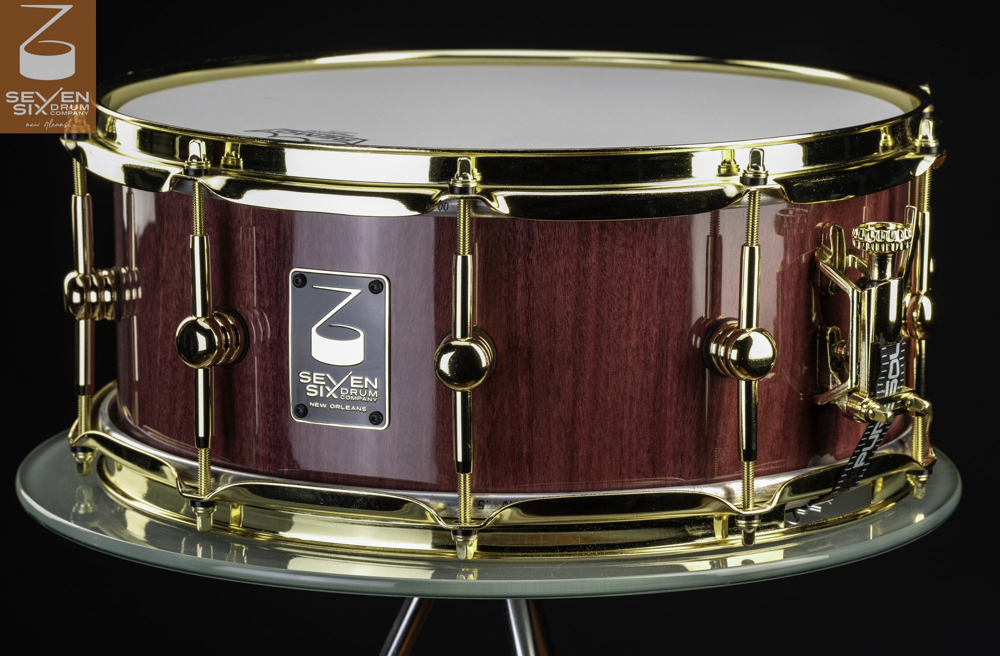 Handmade purple wood snare drum with a high-gloss finish, polished gold hoops, and tube lugs.