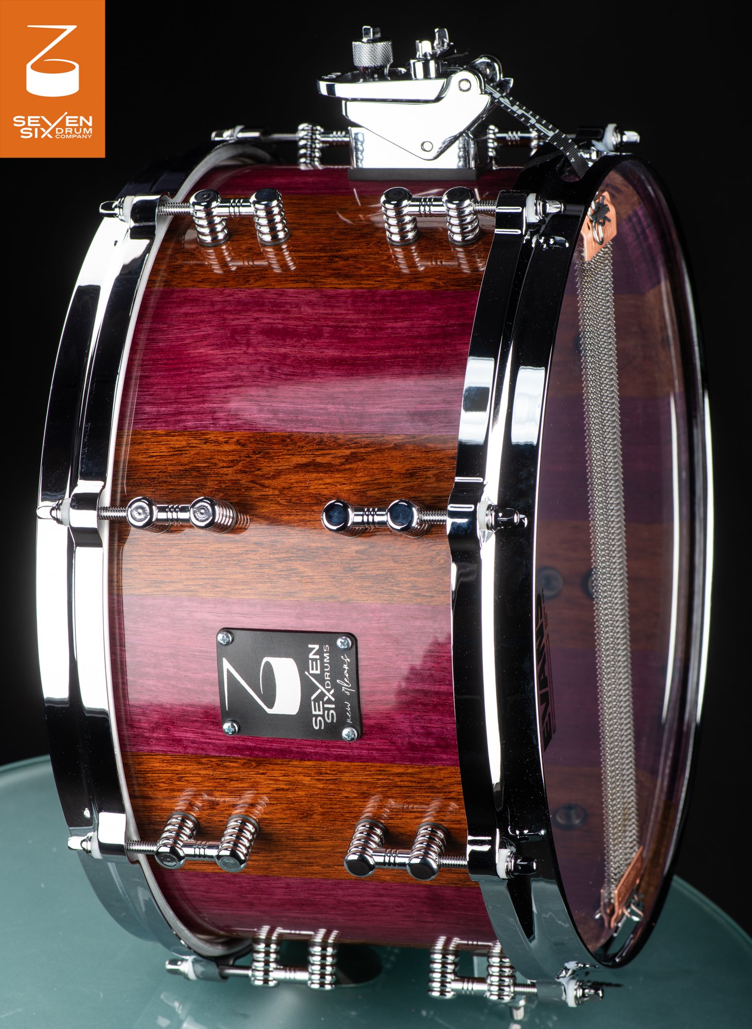 Handmade snare drum with a glossy striped purpleheart and brown wood shell, chrome hoops, and polished tube lugs.