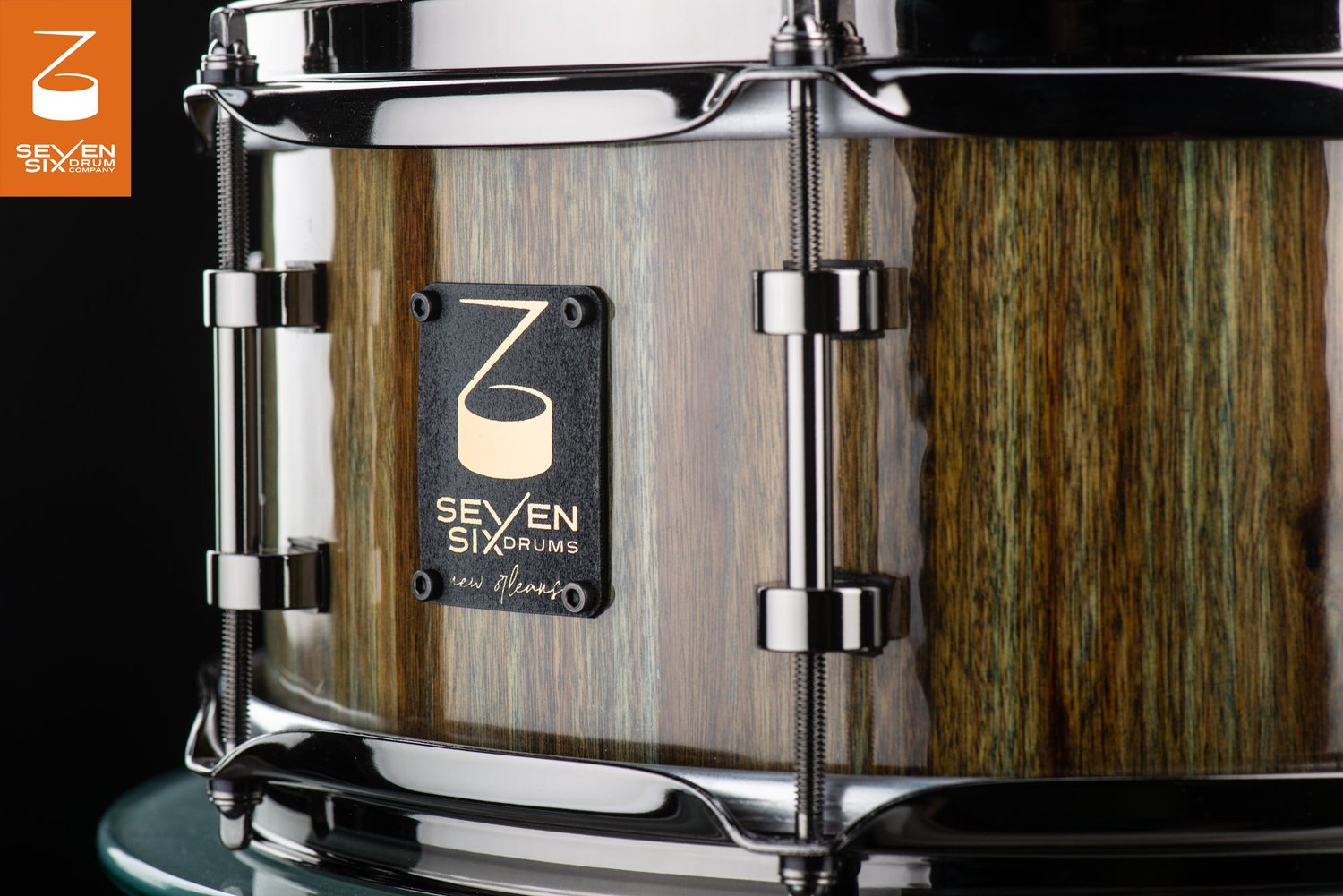 Handmade snare drum featuring a glossy vertical-grain wood shell with black nickel hoops and tube lugs.