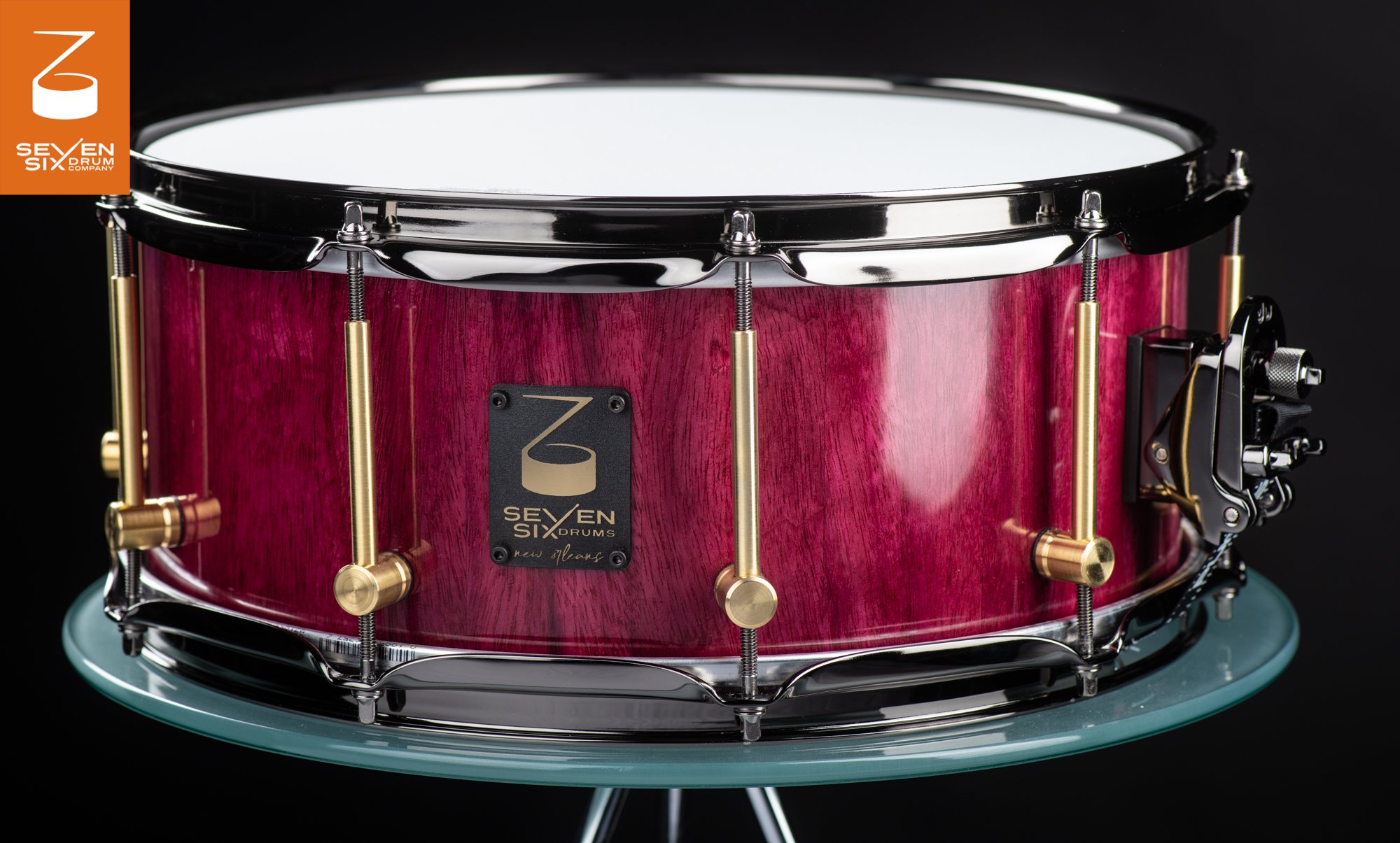 Handmade snare drum with a gloss purple-stained wood shell, brushed brass tube lugs, and dark chrome hoops.