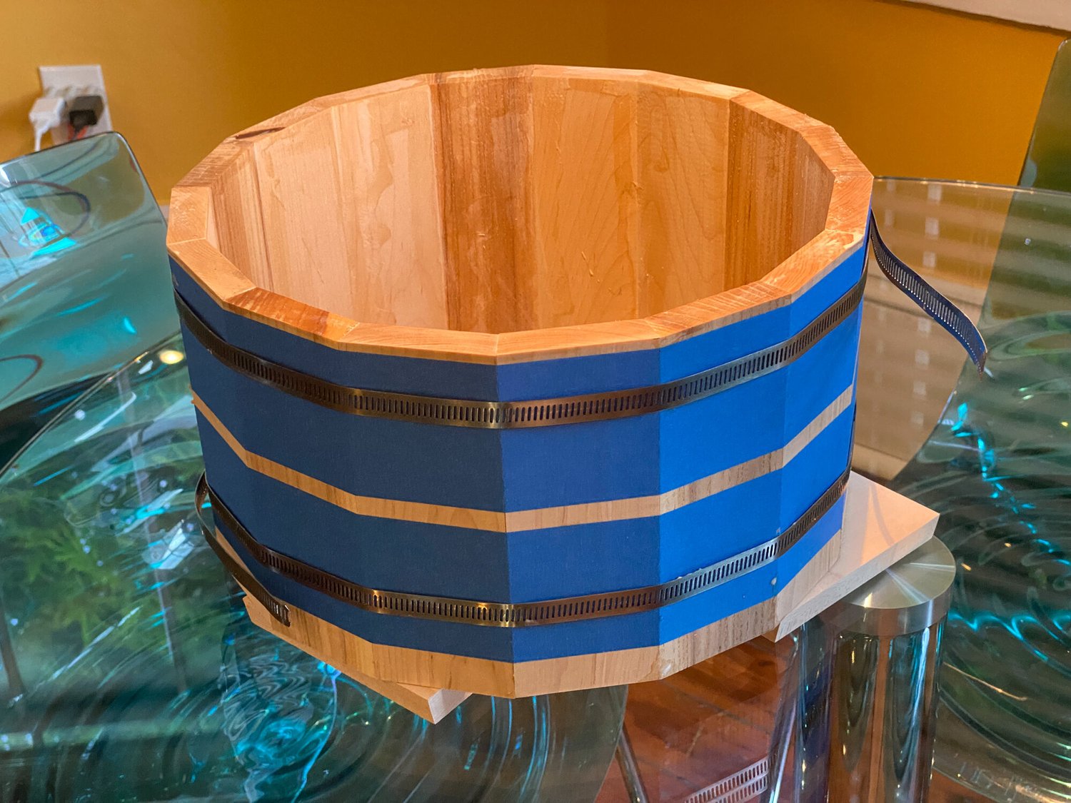 Unfinished light wood stave drum shell secured with blue painter's tape and adjustable metal hose clamps.