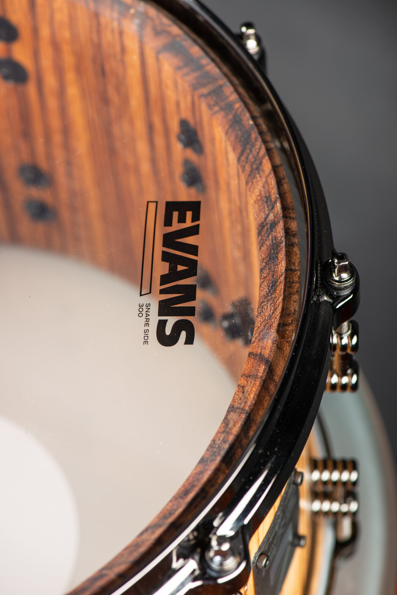 Striped hardwood snare drum with a natural satin finish, clear Evans resonant head, gloss black rim, and chrome tension rods.