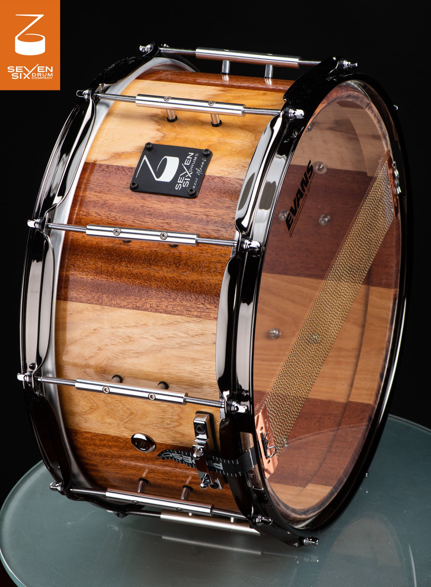 Handcrafted snare drum with a glossy, striped natural wood shell, chrome tube lugs, and black nickel hoops.