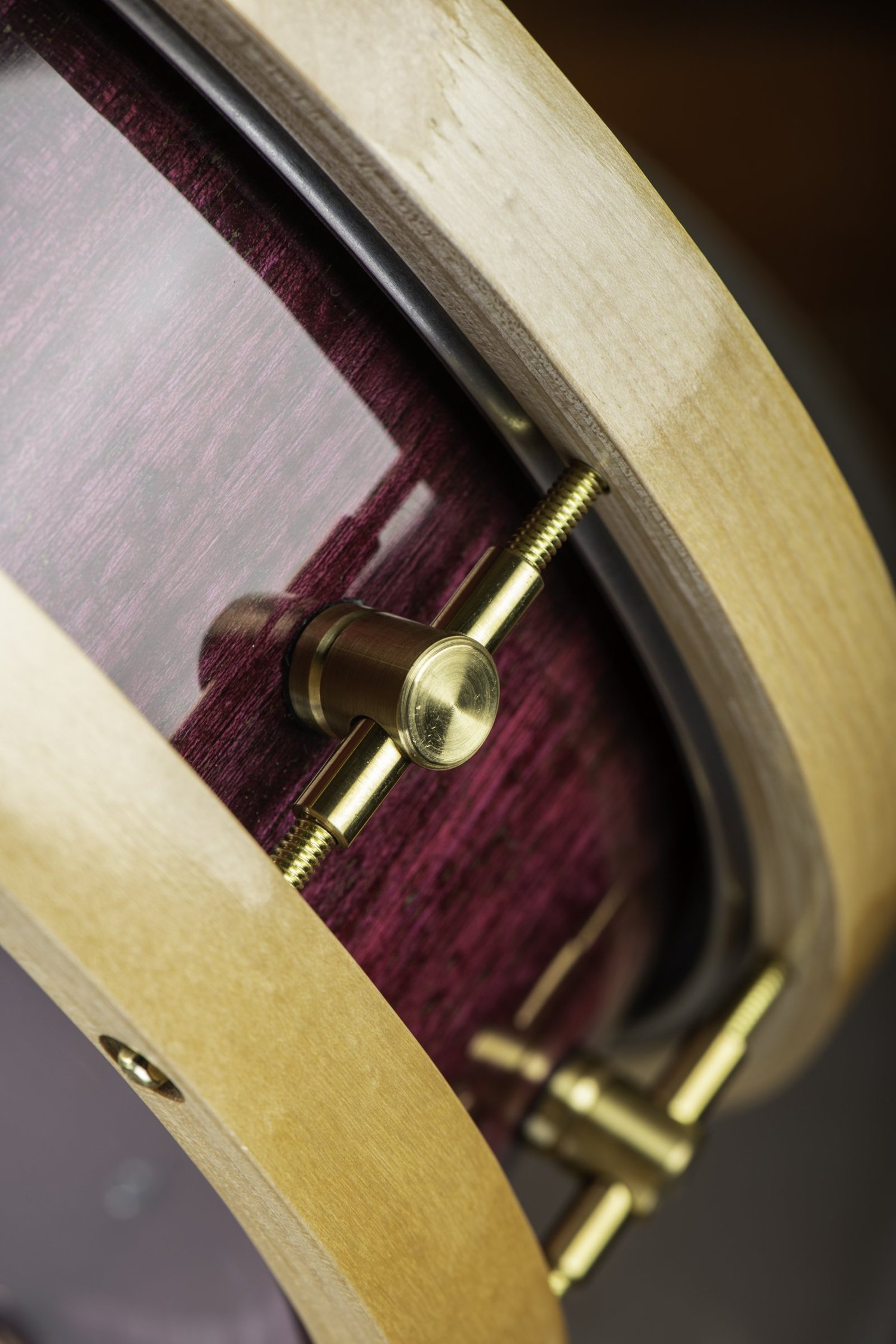 Glossy purple wood snare drum with natural wood hoops and brushed brass lugs.