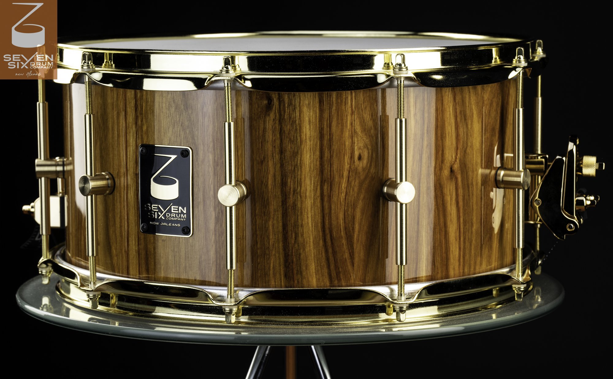 Handcrafted snare drum with a glossy wood grain shell, polished brass hoops, and center-mounted brass lugs.