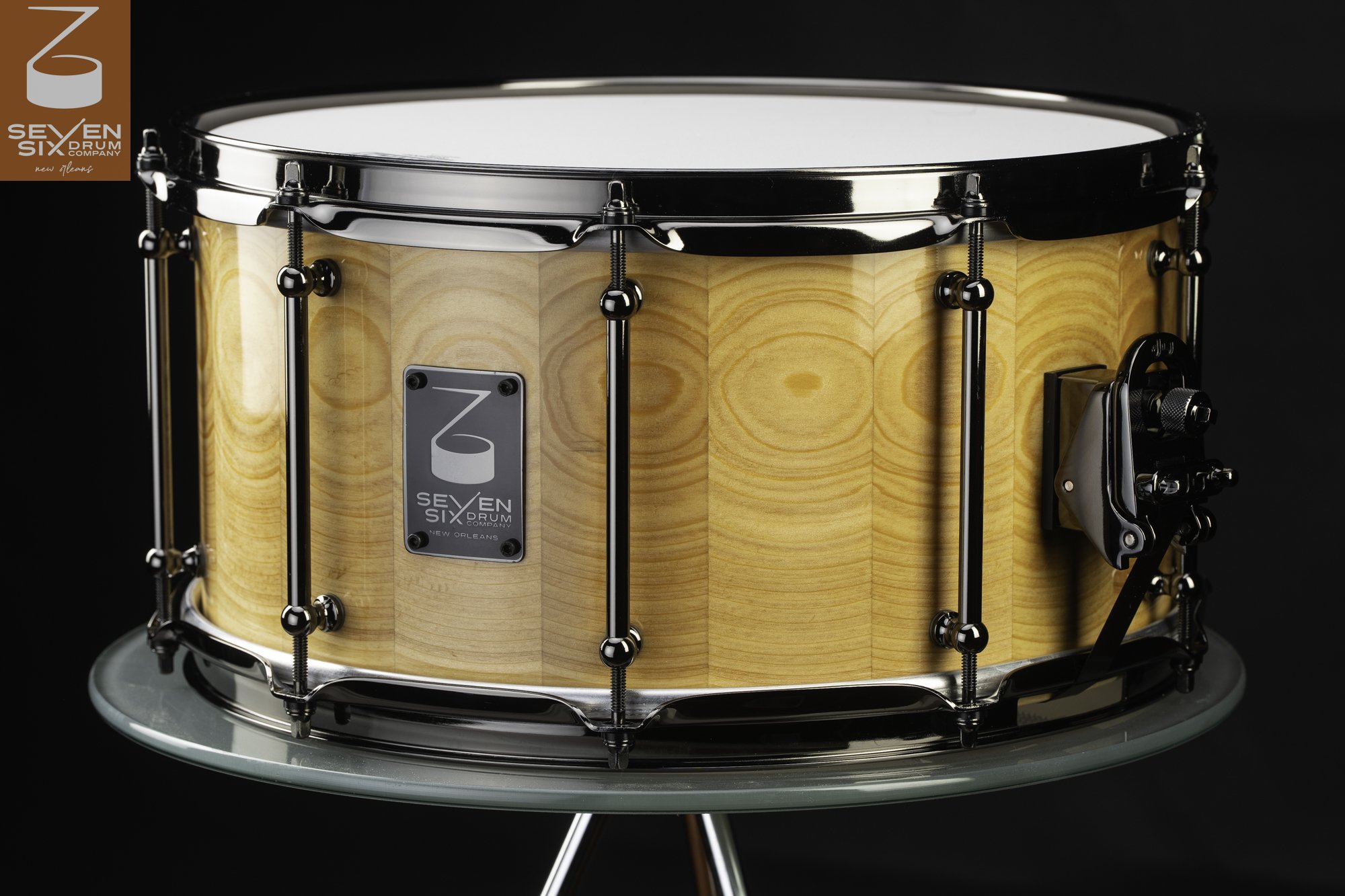Handmade snare drum featuring a glossy natural stave wood shell, black nickel tube lugs, and matching hoops.