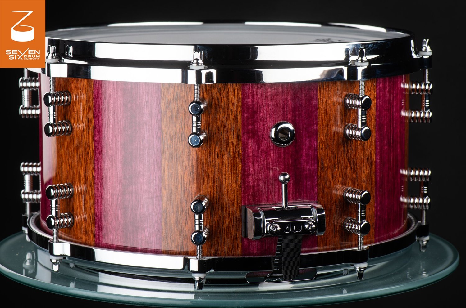 Handmade snare drum with glossy purpleheart and brown wood stripes, polished chrome hoops, and a DW throw-off.