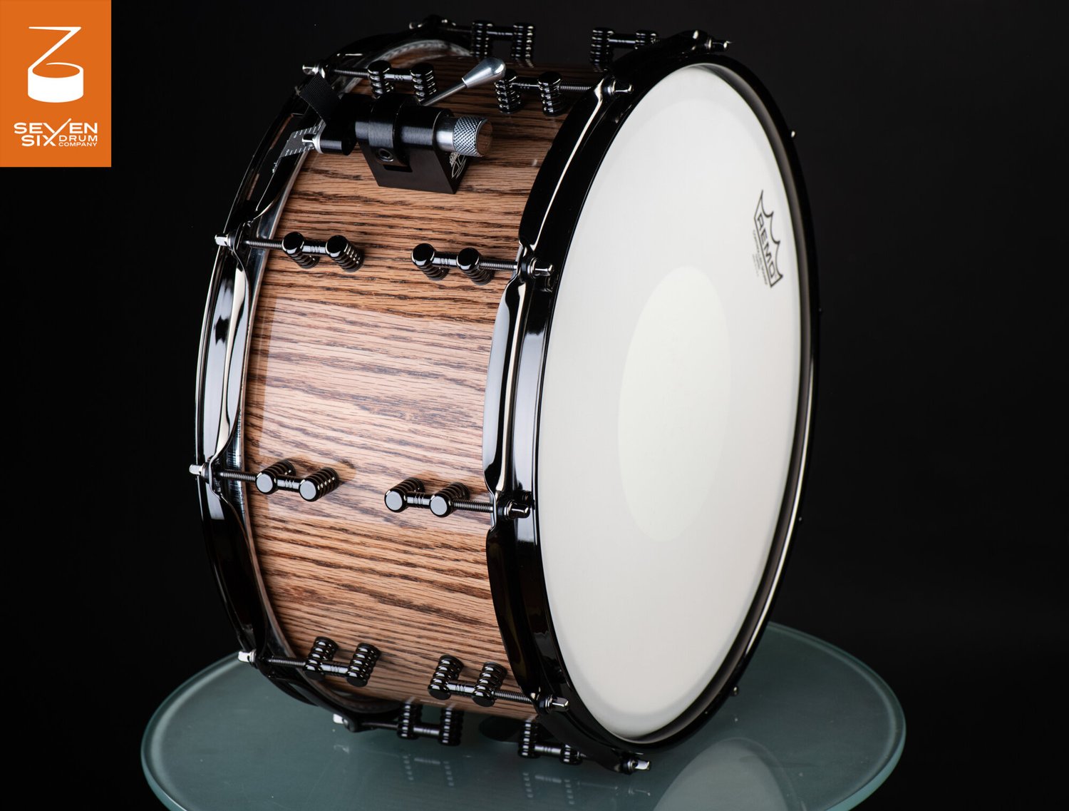 Deep snare drum with a glossy natural wood shell, black hoops, segmented black lugs, and a white coated head.