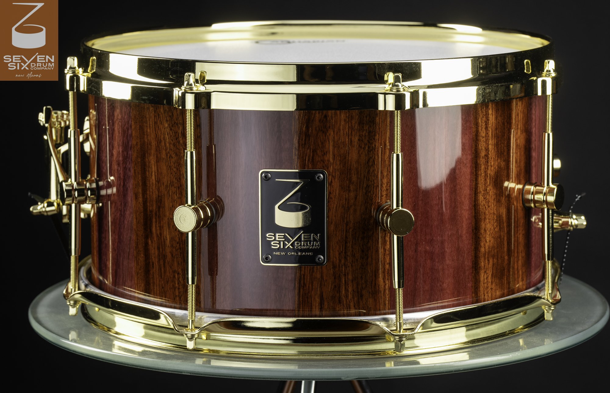 Handmade snare drum featuring a glossy reddish-brown wood shell with polished gold hoops and hardware.