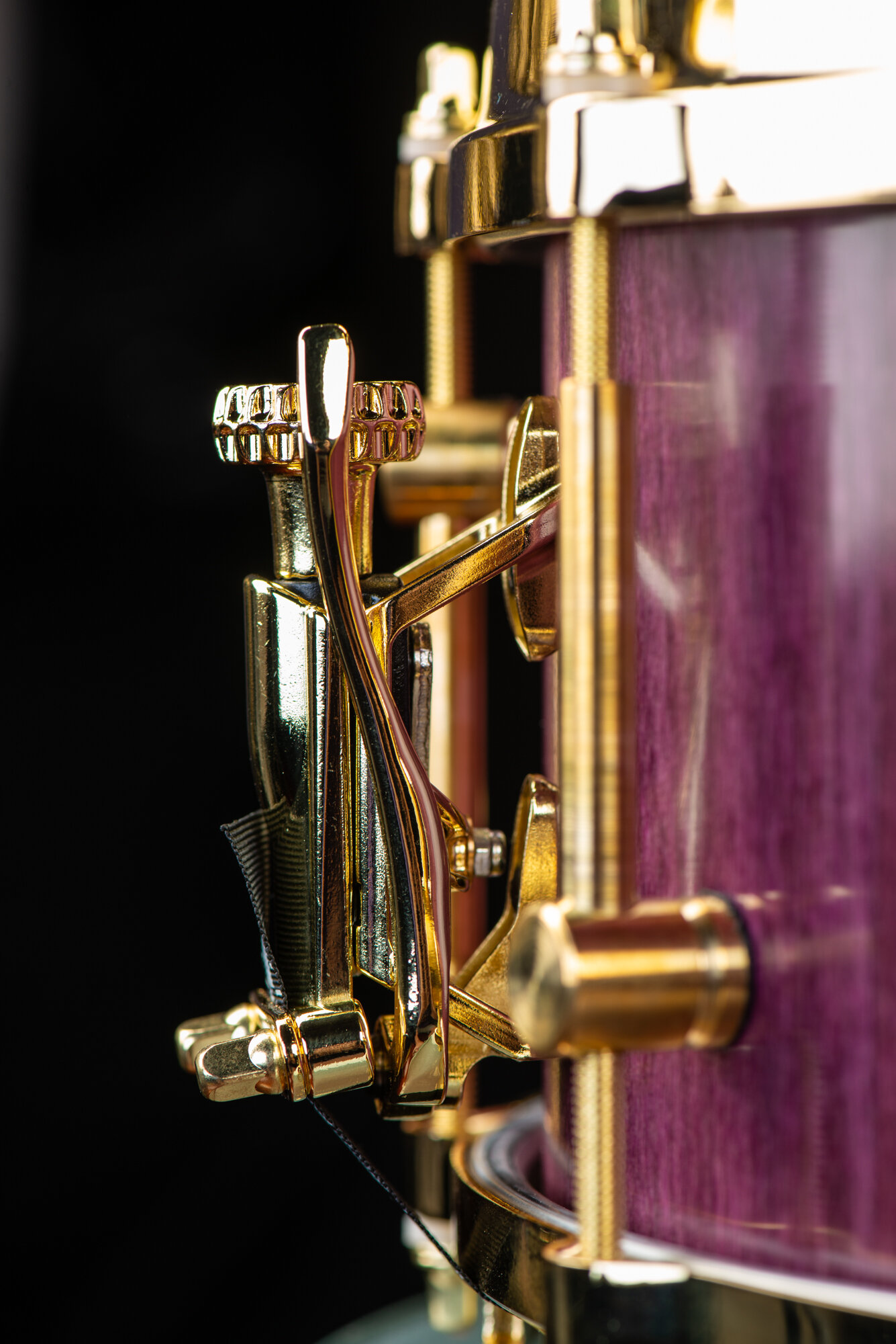 Purple wood snare drum featuring a polished gold throw-off strainer and matching gold hardware.