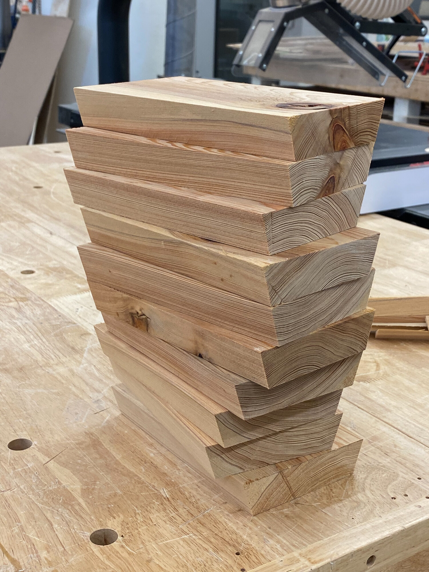 Stack of unfinished beveled wood staves with visible end grain, cut to construct a stave snare drum shell.