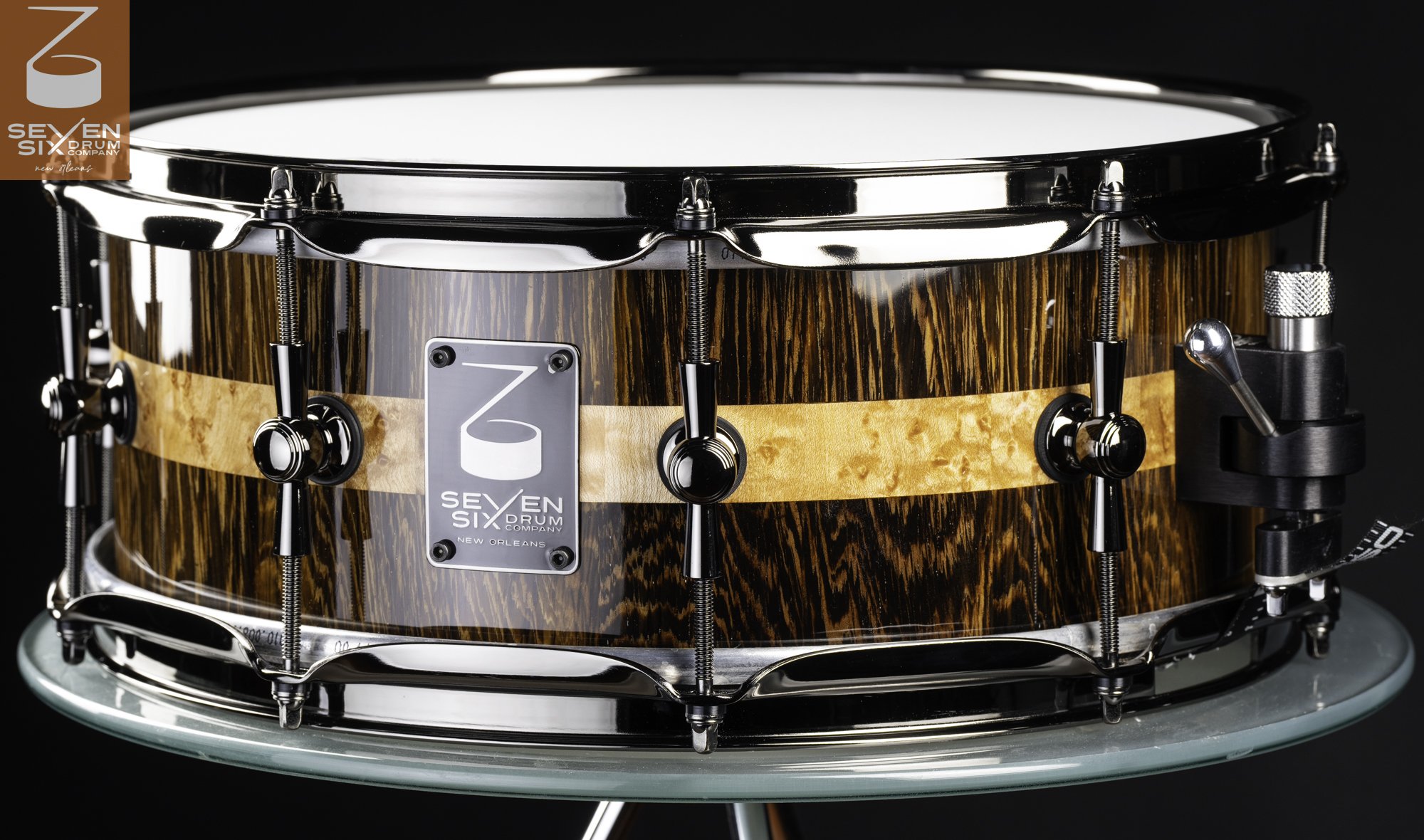 Handmade snare drum in glossy dark wood with a blonde burl inlay stripe and polished black nickel hardware.