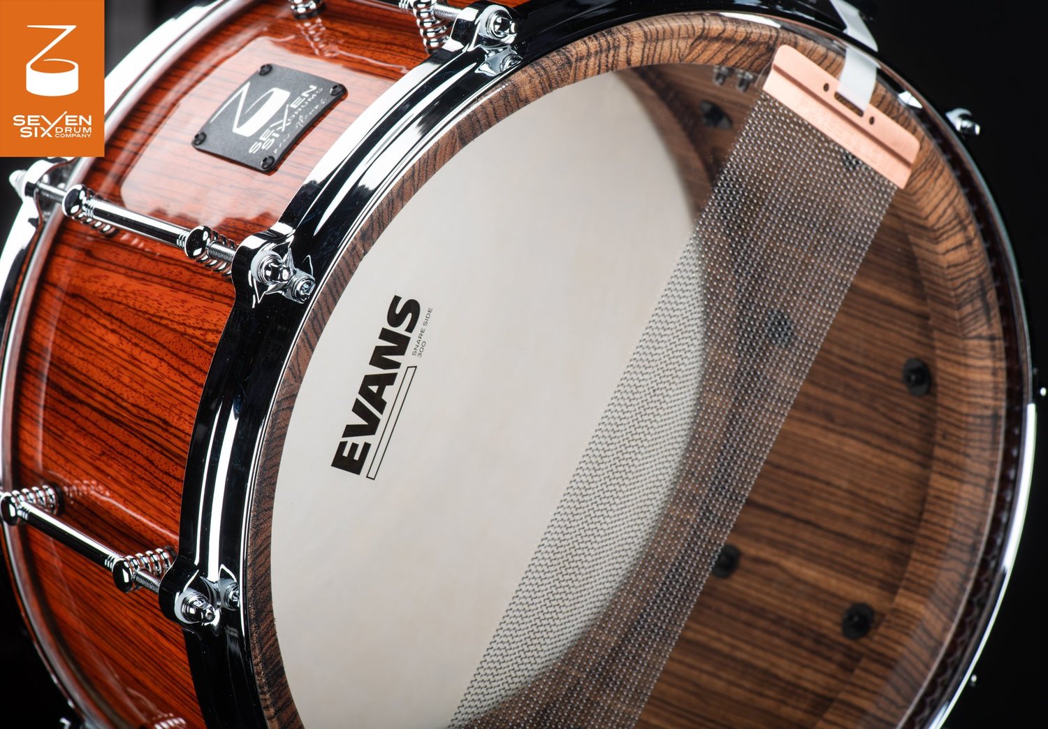 Handmade snare drum featuring a glossy wood shell, chrome tube lugs, and snare wires over an Evans bottom head.