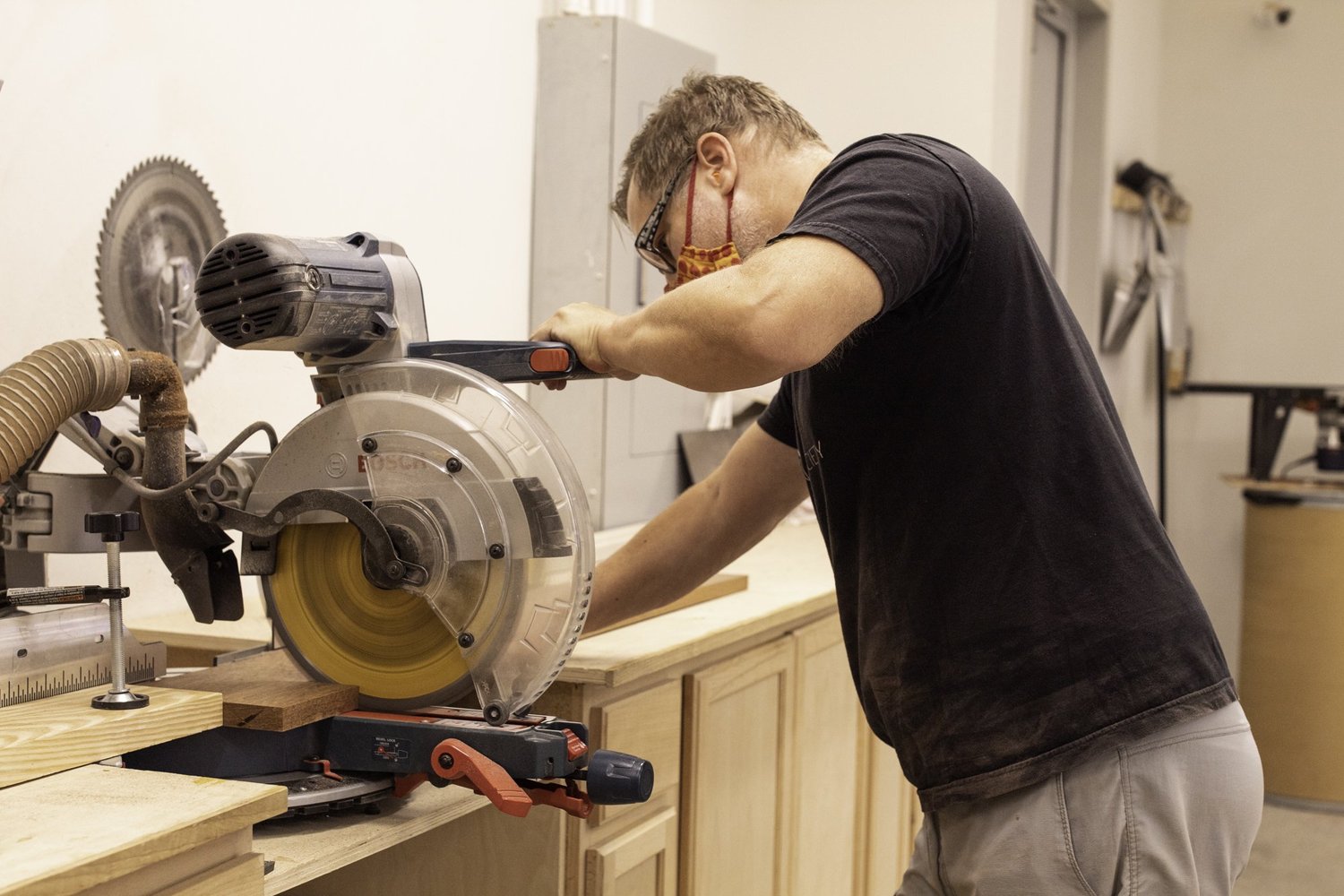 A craftsman cuts an unfinished hardwood block using a Bosch sliding miter saw in a workshop.