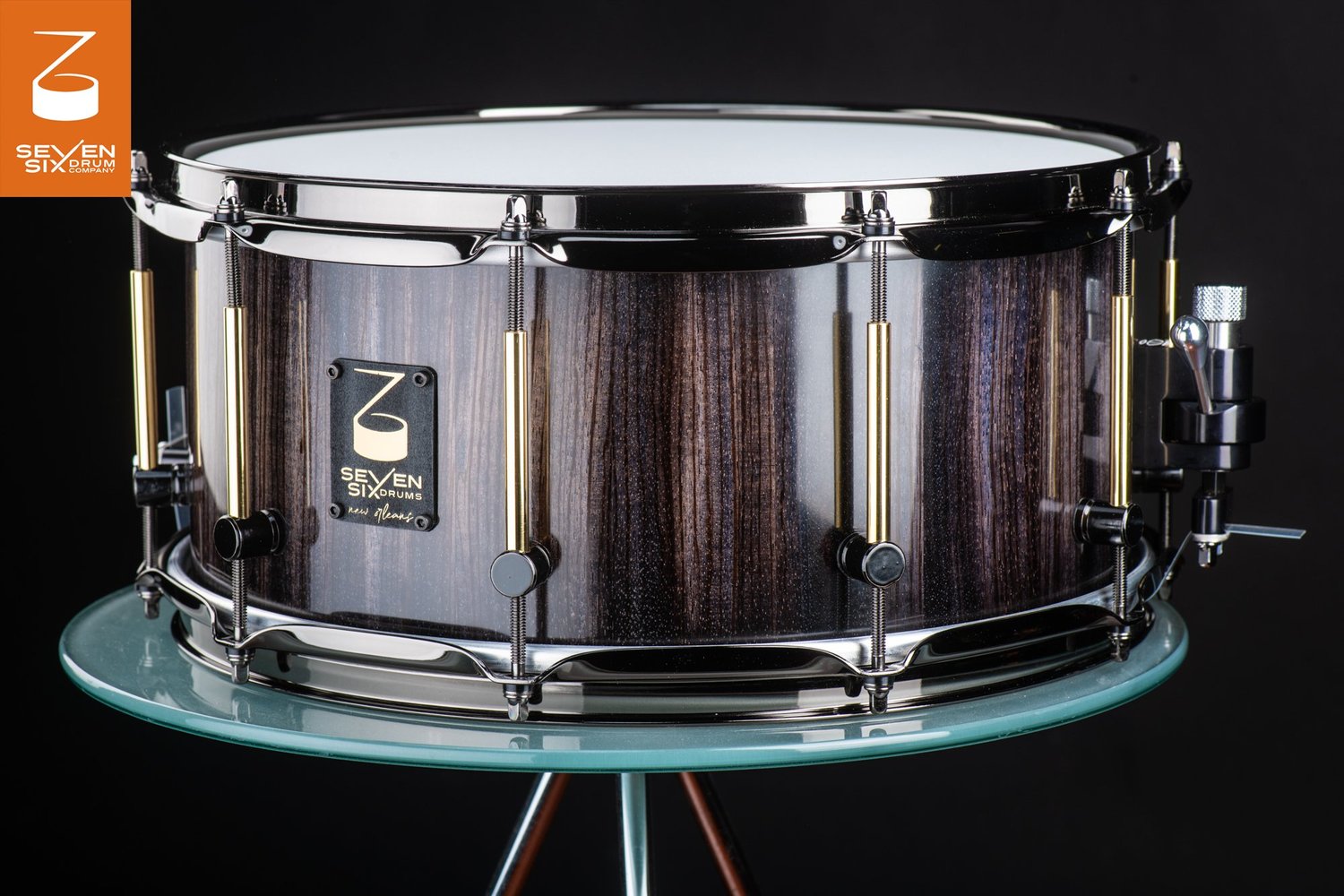 Handmade snare drum featuring a dark vertical-grain wood shell, brass tube lugs, and polished black nickel hoops.