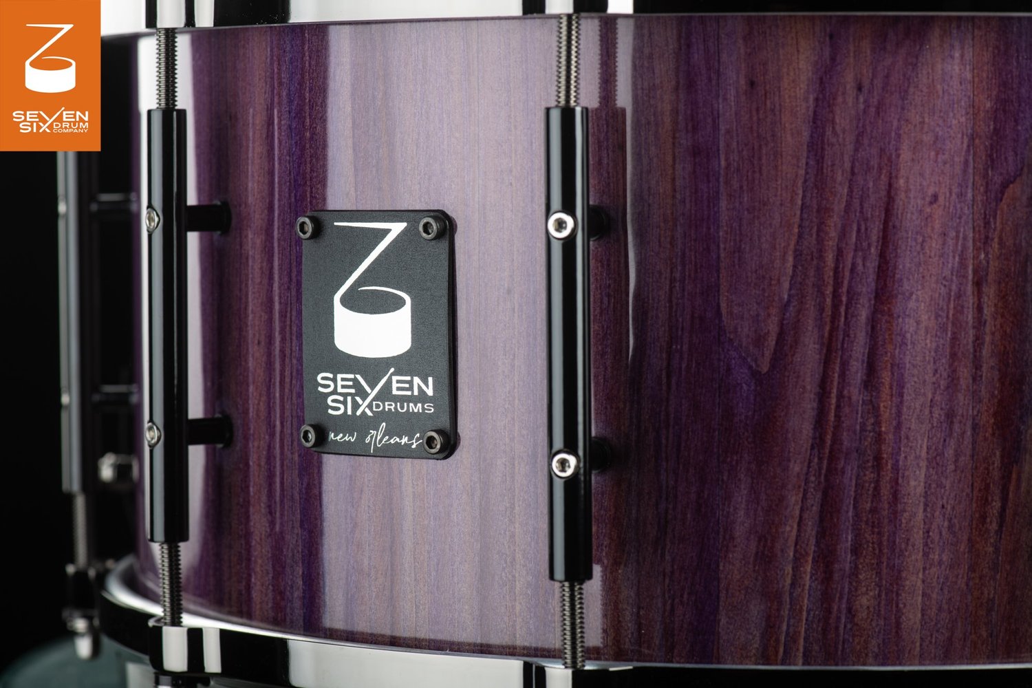 Glossy purple wood snare drum featuring black tube lugs, chrome hoops, and a black Seven Six Drums badge.